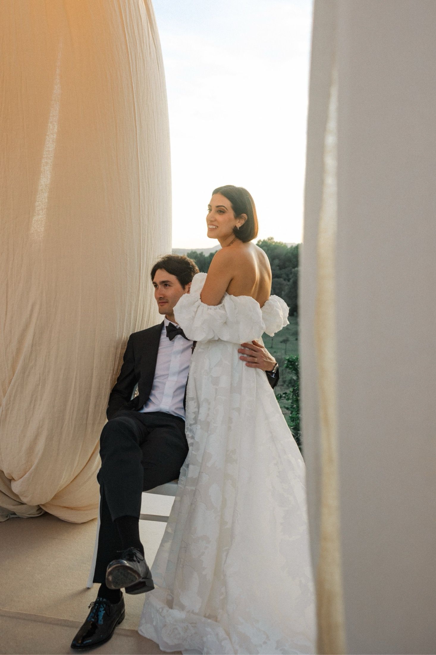 A bride and groom share an intimate moment between white curtains during their wedding photoshoot.