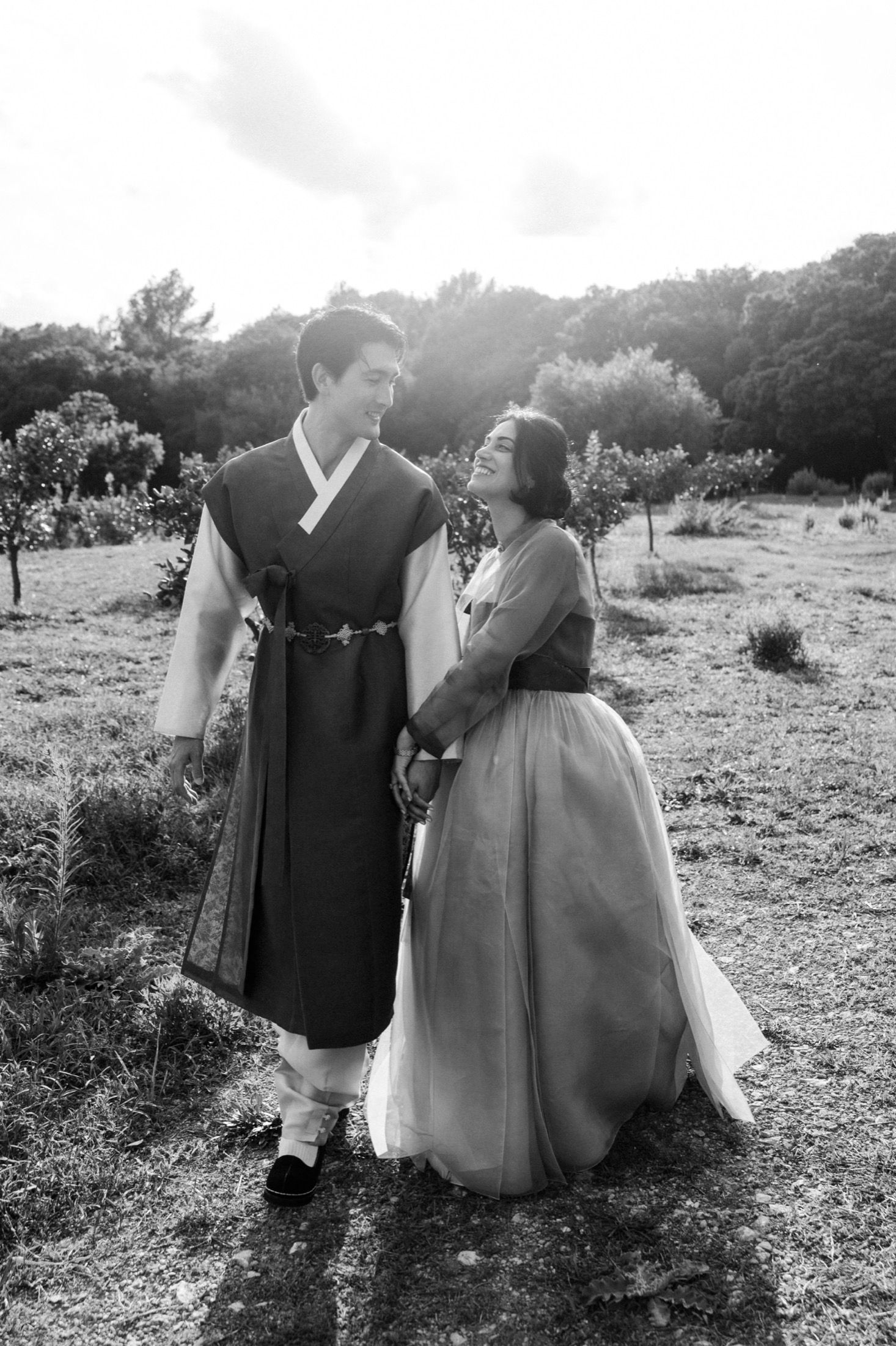 A couple in traditional Korean hanbok attire poses together in a scenic outdoor setting during a photo session.