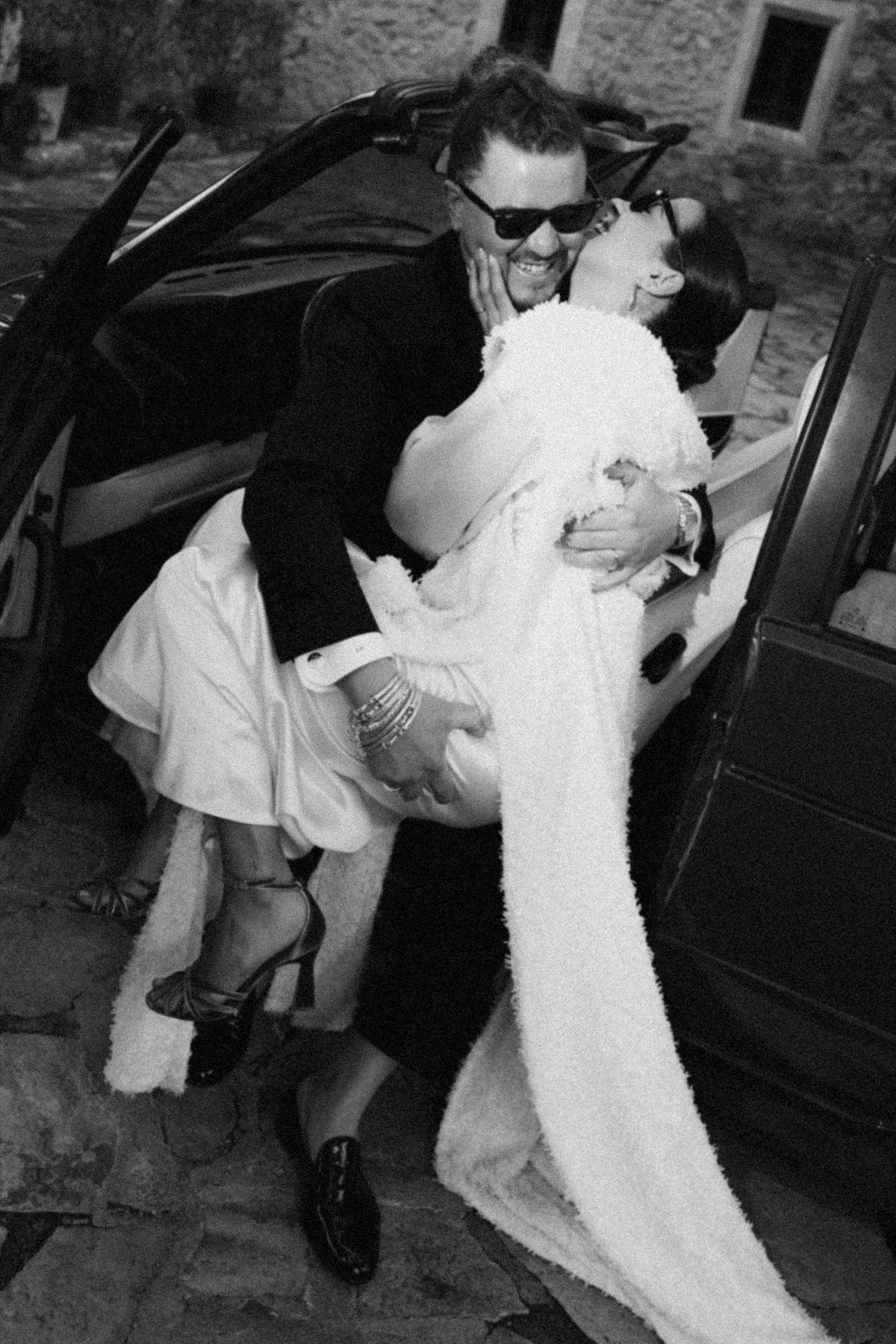 A couple shares a romantic moment in black and white near their wedding car.