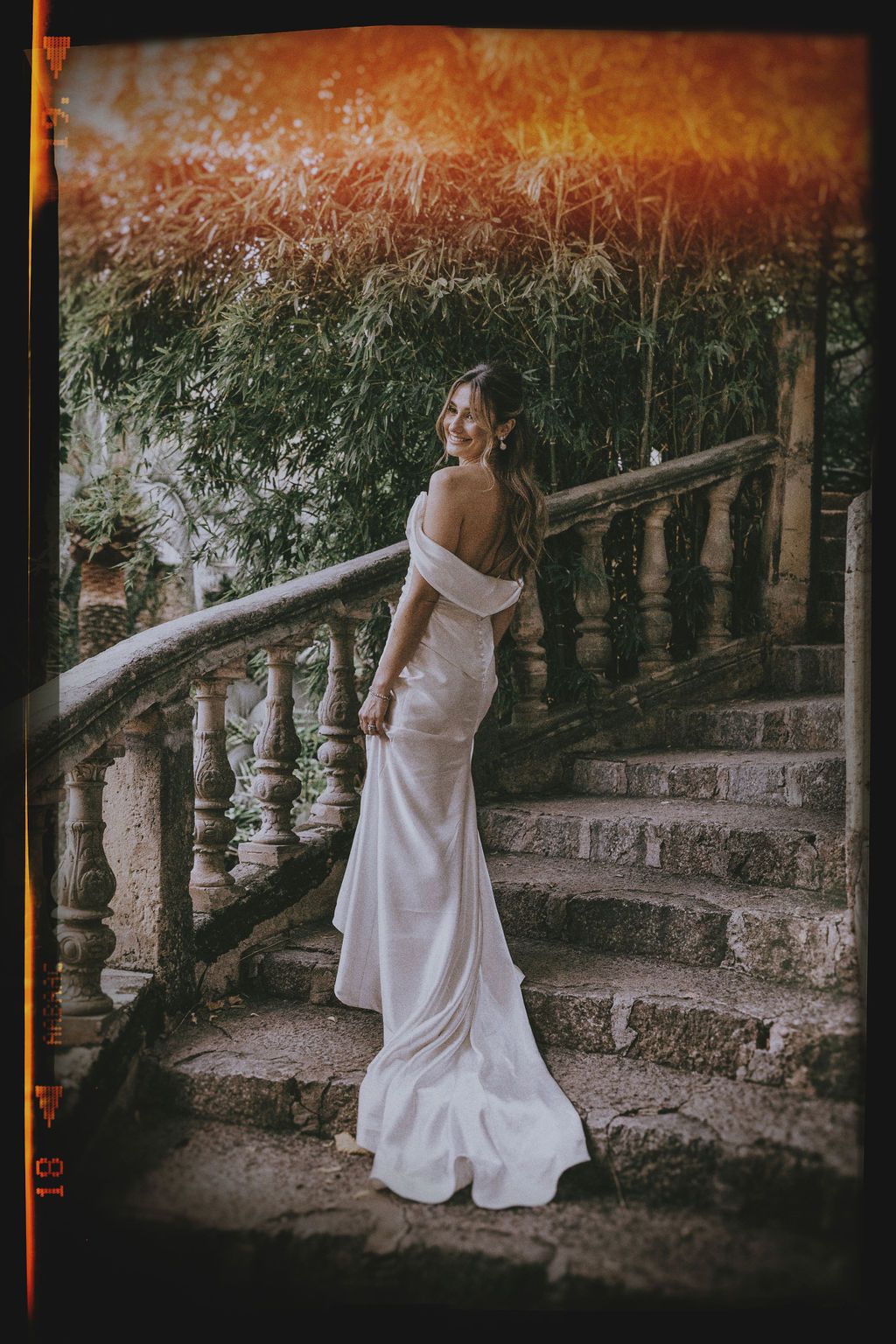 Artistic sequence of a bride in white dress moving along stone balustrade in warm sunset lighting.