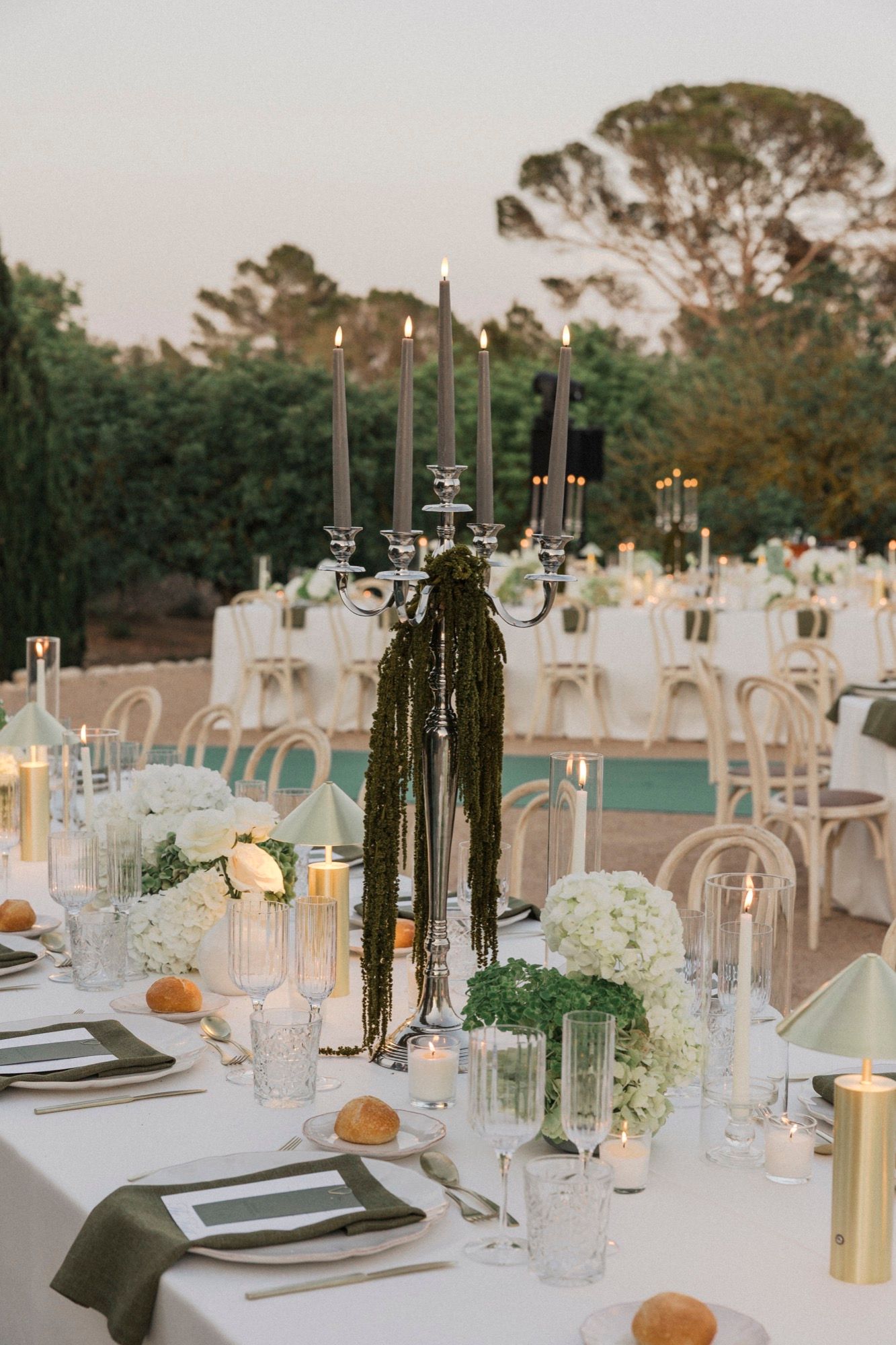 Wedding table settings with black candles, crystal glassware, and white linens at dusk.