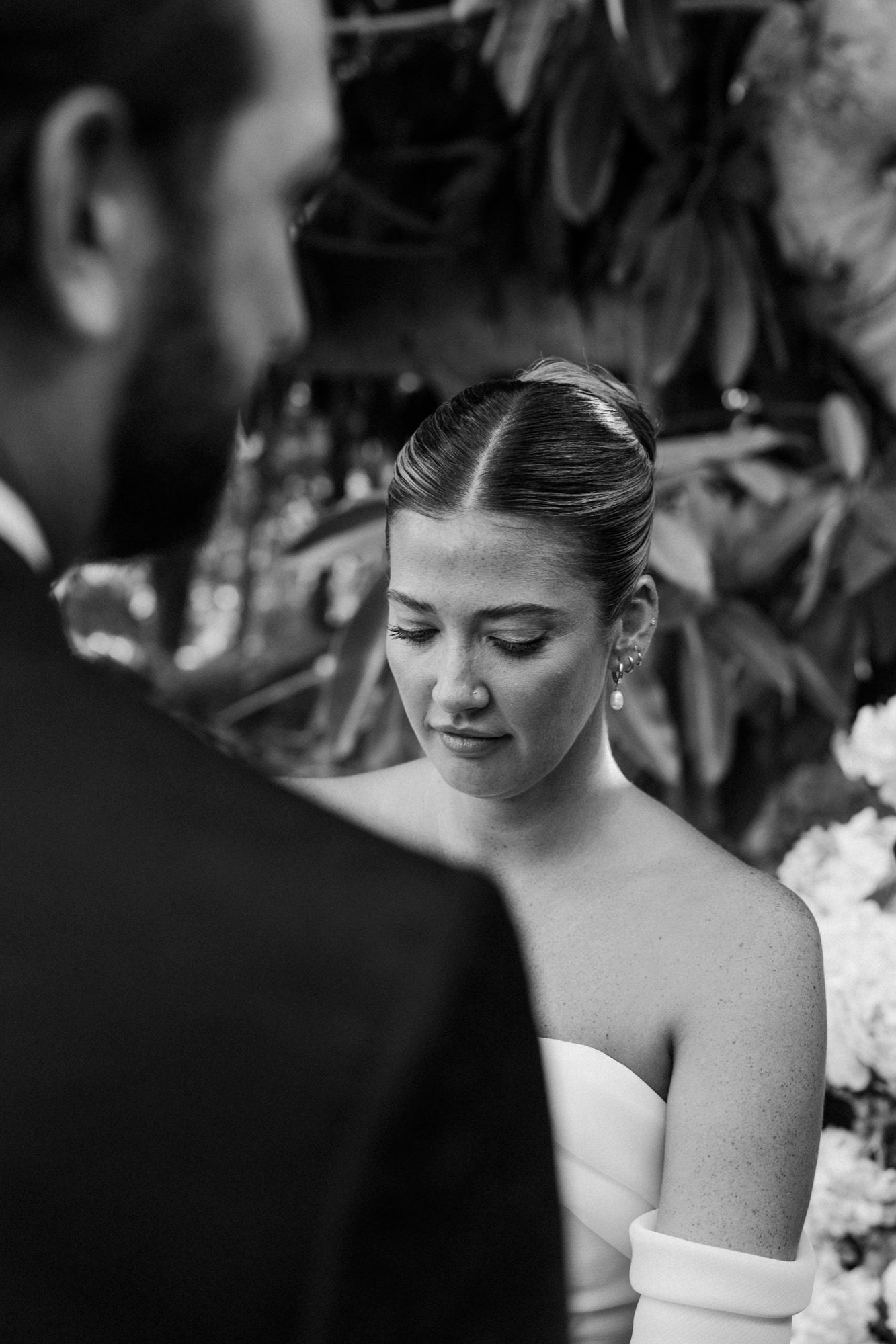 Intimate black and white wedding ceremony portrait with white floral backdrop.