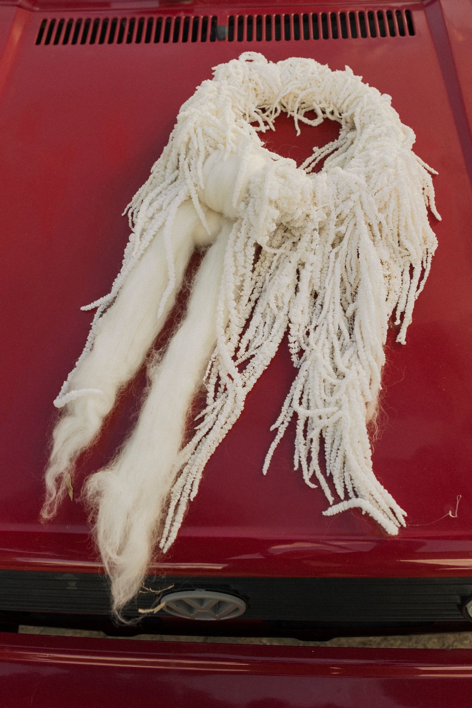 White fringed wedding accessory artistically displayed on red car hood.