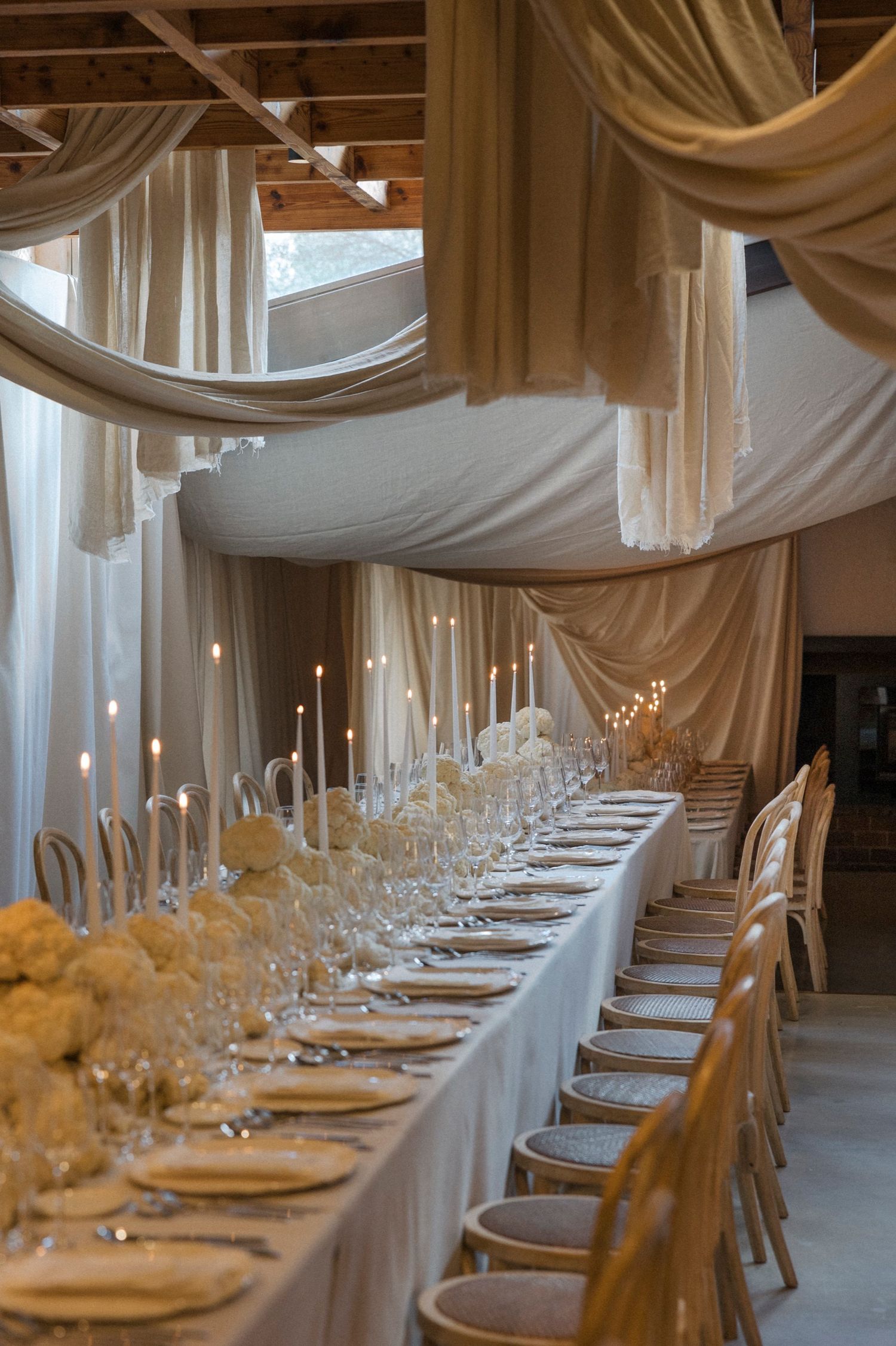 Long dining table with white linens and gold chairs set beneath dramatic draped fabric ceiling.