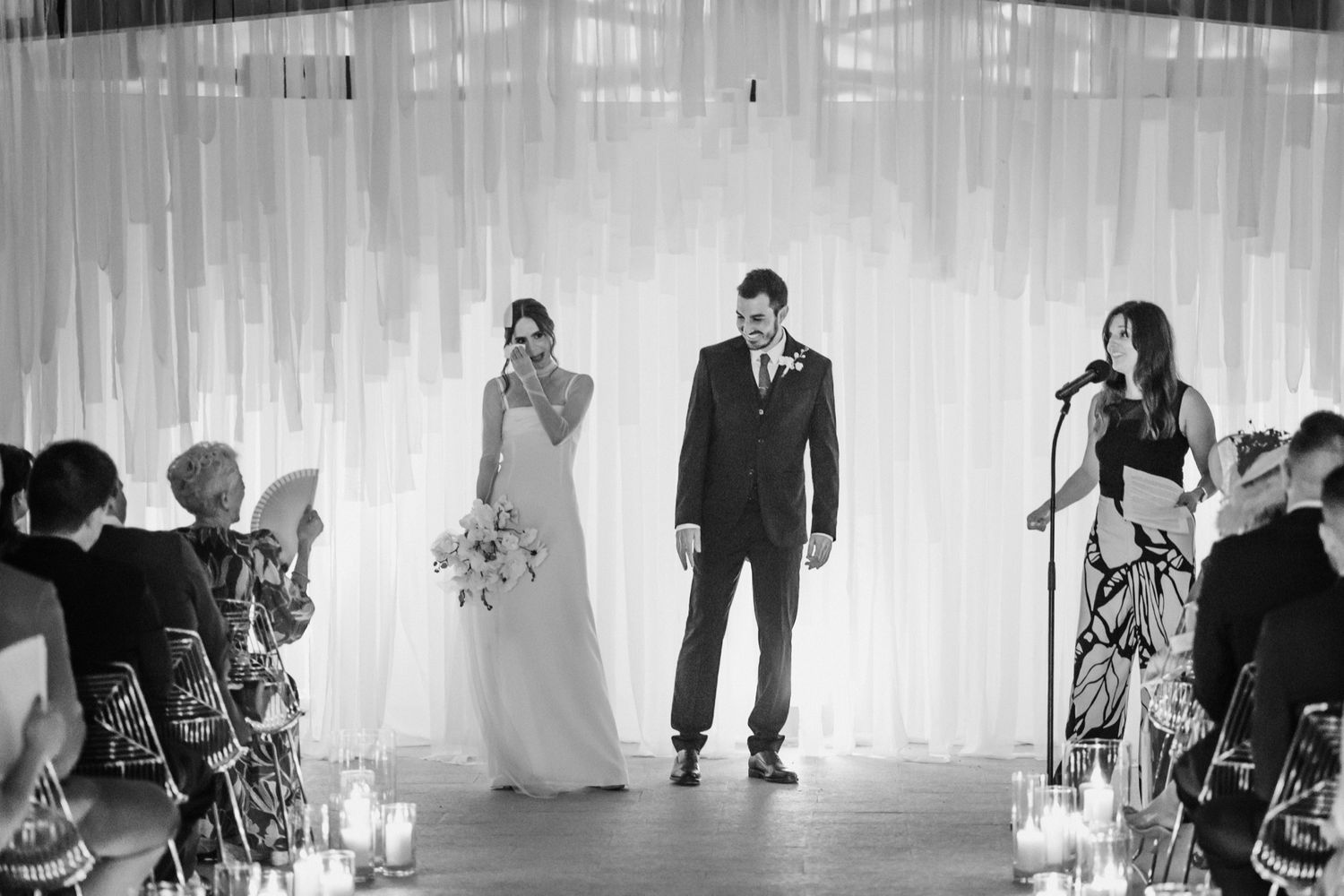 A panoramic black and white photo of a wedding ceremony setup with chairs, decor and guests in an indoor venue.