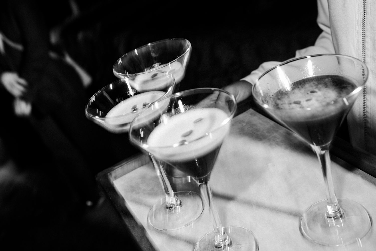 A row of martini glasses filled with cocktails sits on a dark bar counter with dramatic lighting.