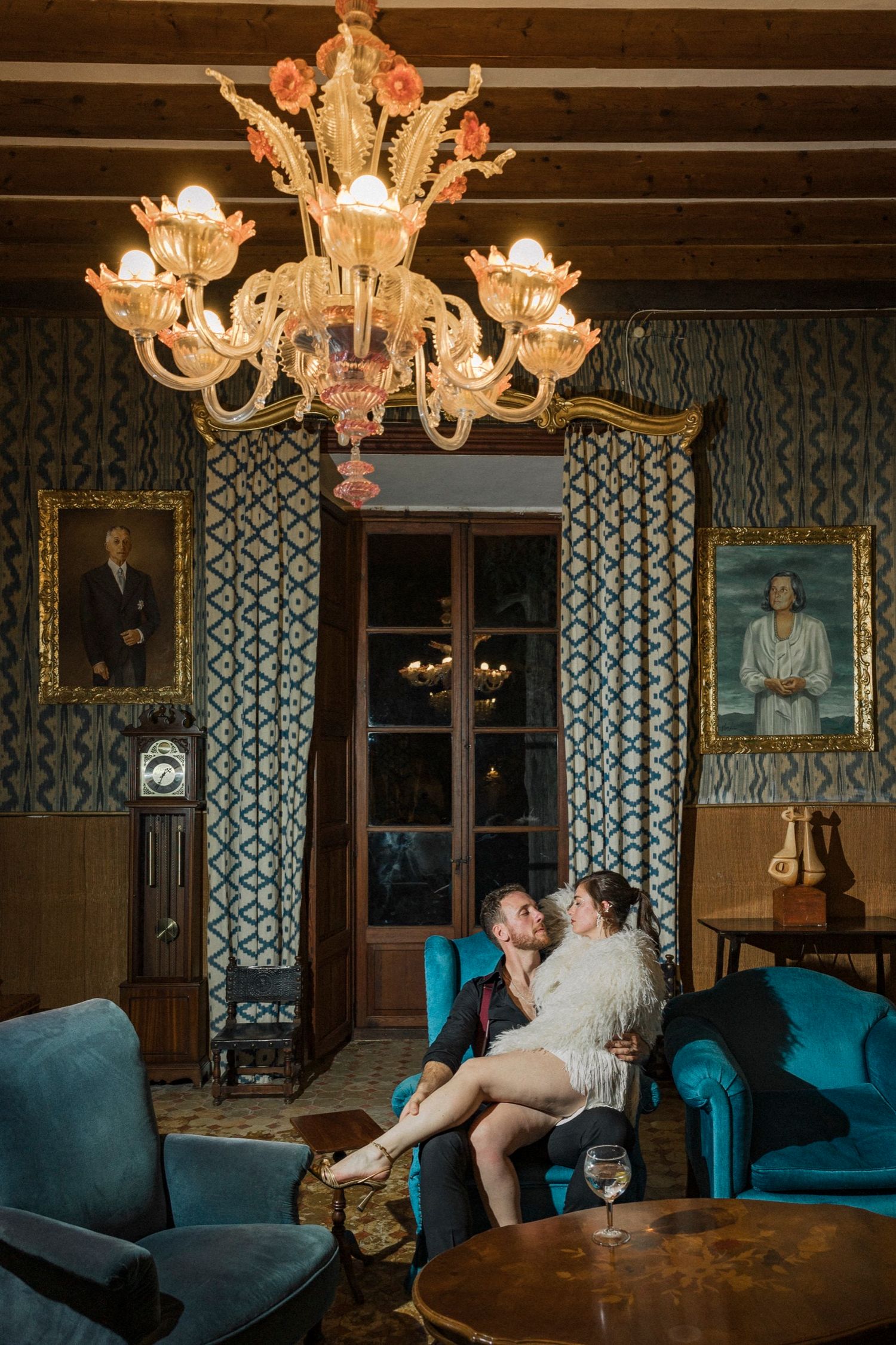 Elegant chandelier illuminates a vintage room with blue velvet furniture and patterned wallpaper in a sequence of photos.
