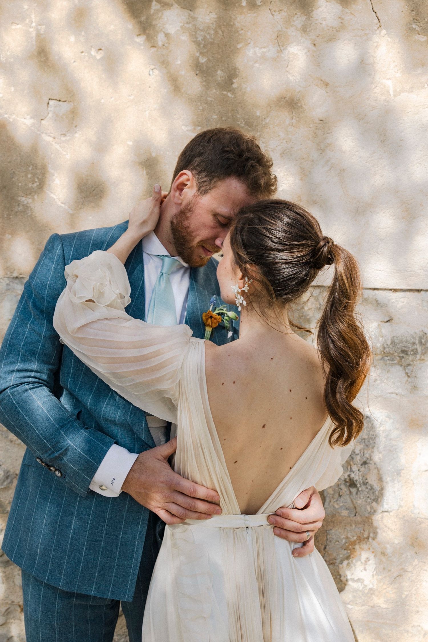 Romantic wedding couple embraces against textured wall in series of intimate dance-like poses.
