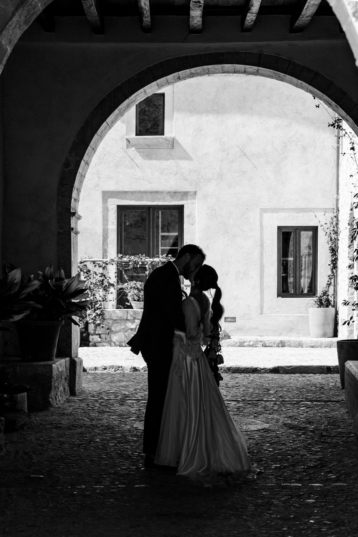 People in period dress walk through a series of stone archways in a historic courtyard setting.
