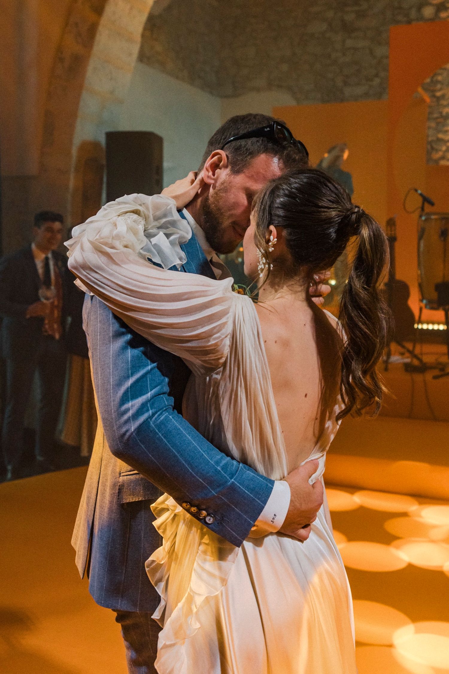 A couple shares an intimate dance moment on their wedding day, illuminated by warm amber lighting in the reception venue.