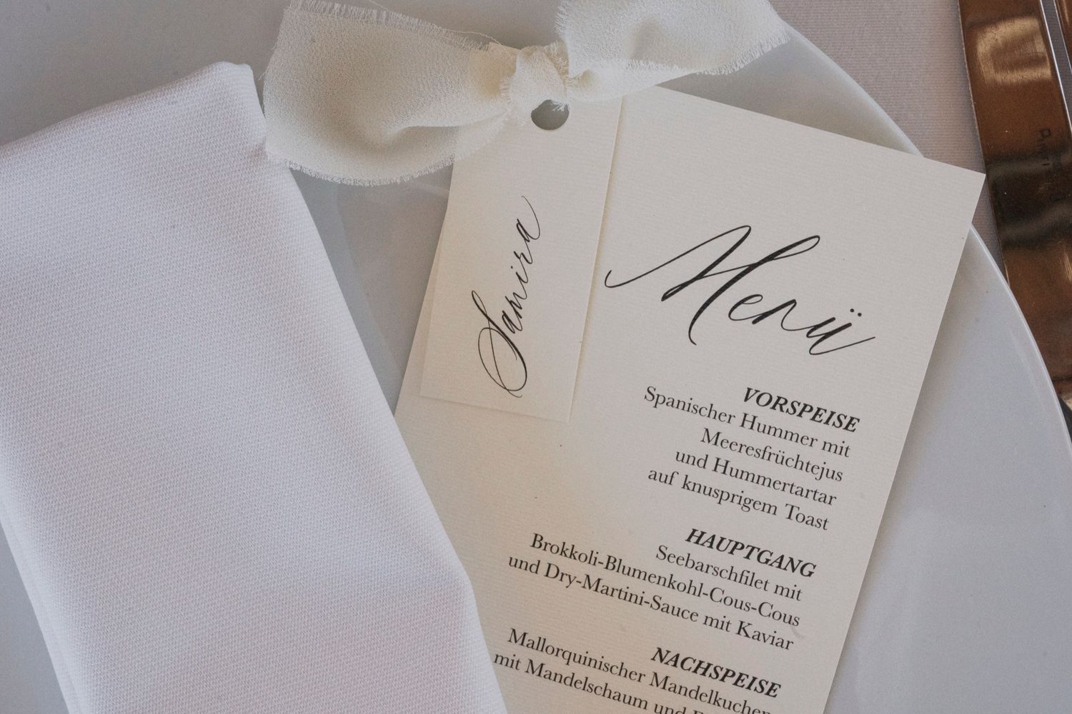 Elegant wedding menu card with cursive script displayed beside a white folded napkin at a formal dinner setting.