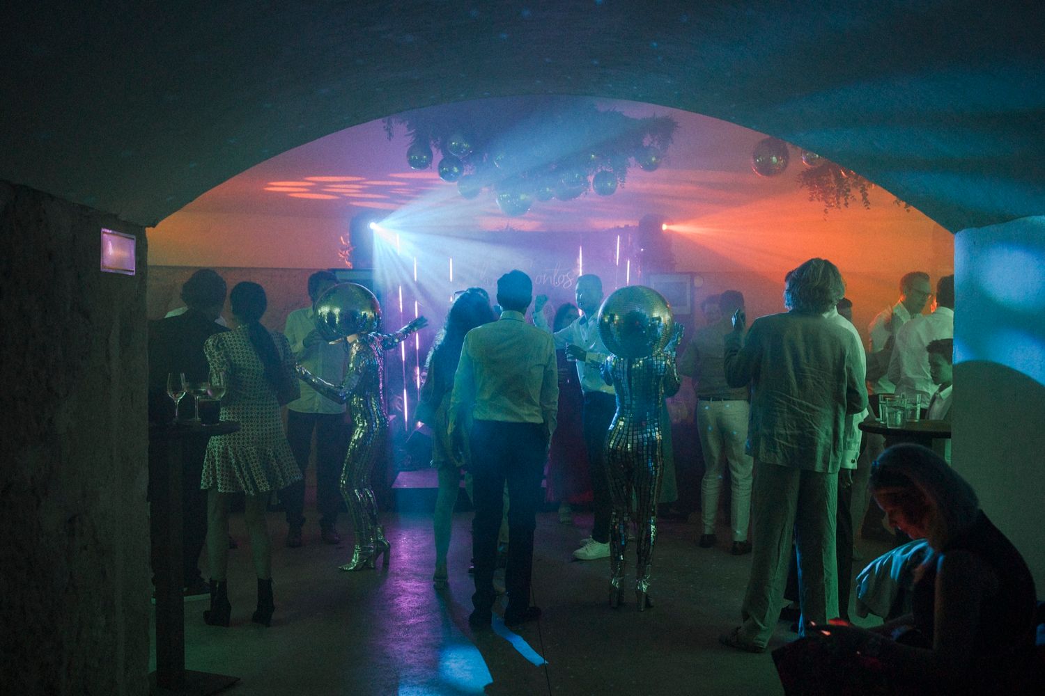 People dancing in a dimly lit nightclub with colorful neon lights and arched ceilings.