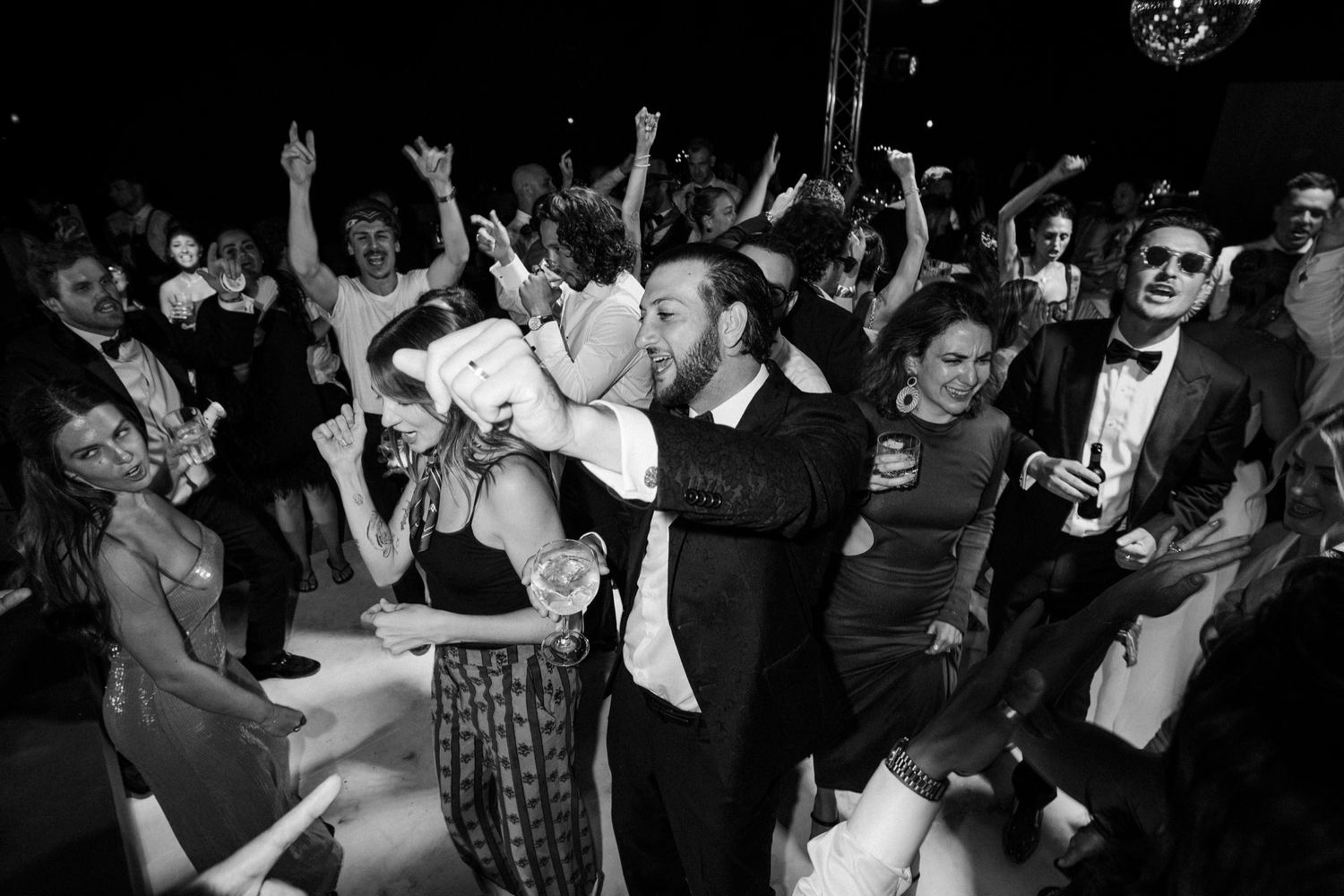 Wedding guests dance and celebrate as groom lifts bride during lively reception party.