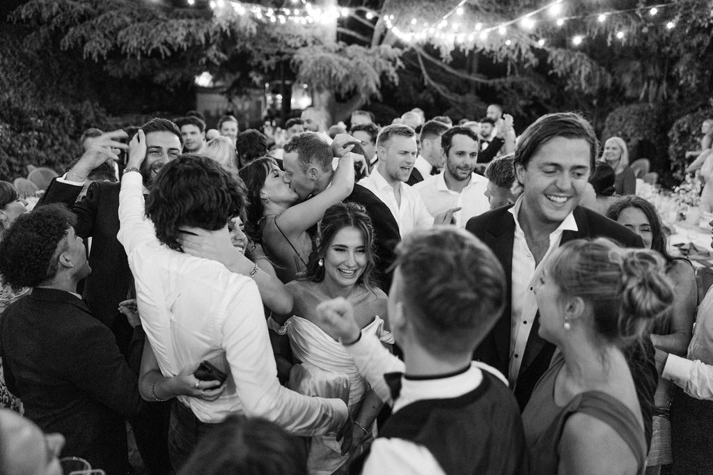 Crowded dance floor at an outdoor wedding reception with string lights overhead.