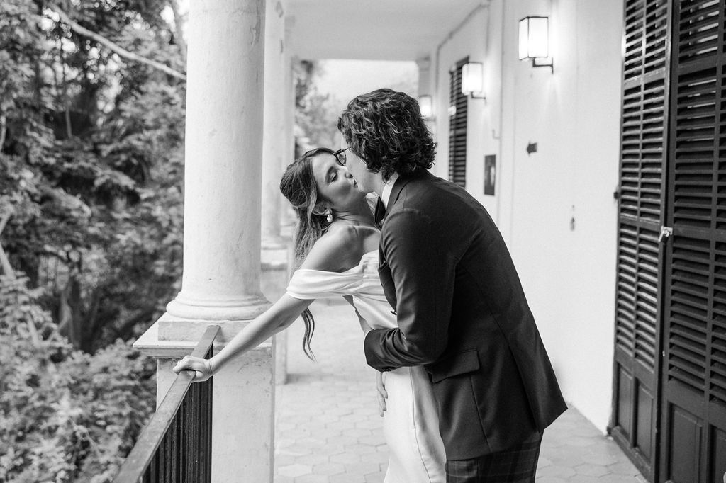 Romantic couple embraces on an elegant columned porch during their wedding photoshoot.