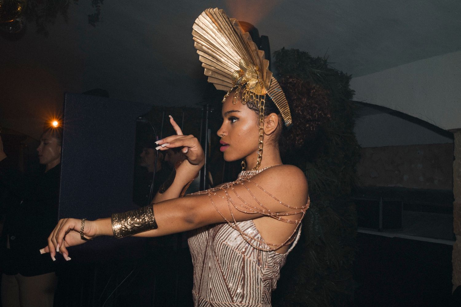 Woman in Egyptian-inspired gold costume with fan headdress and chain jewelry posing at a glamorous event.