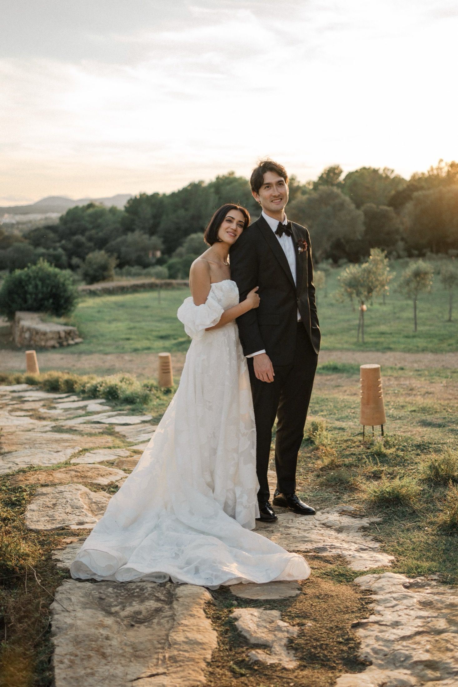 Newlyweds pose together on a stone pathway surrounded by natural landscape during golden hour.