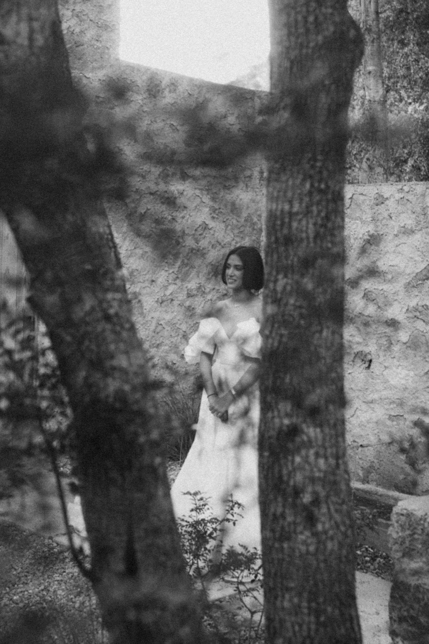 Artistic black and white photos of a figure in a white dress among trees creating shadowy silhouettes.