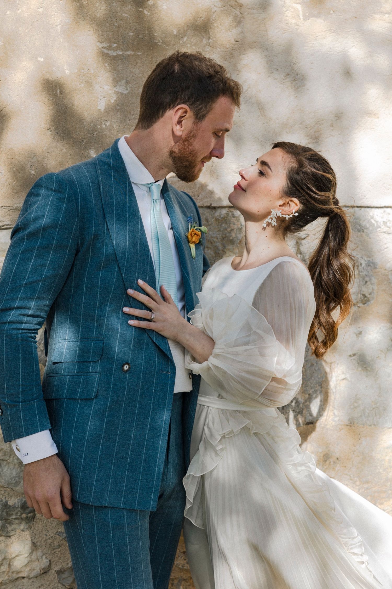 A romantic wedding couple in white dress and blue checkered suit embrace against a textured wall in multiple poses.