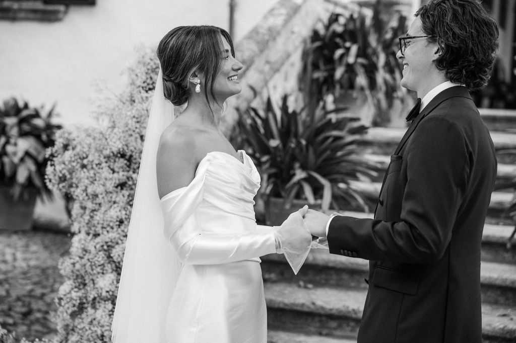 A black and white wedding photo showing a tender moment between a couple in formal attire during their ceremony.