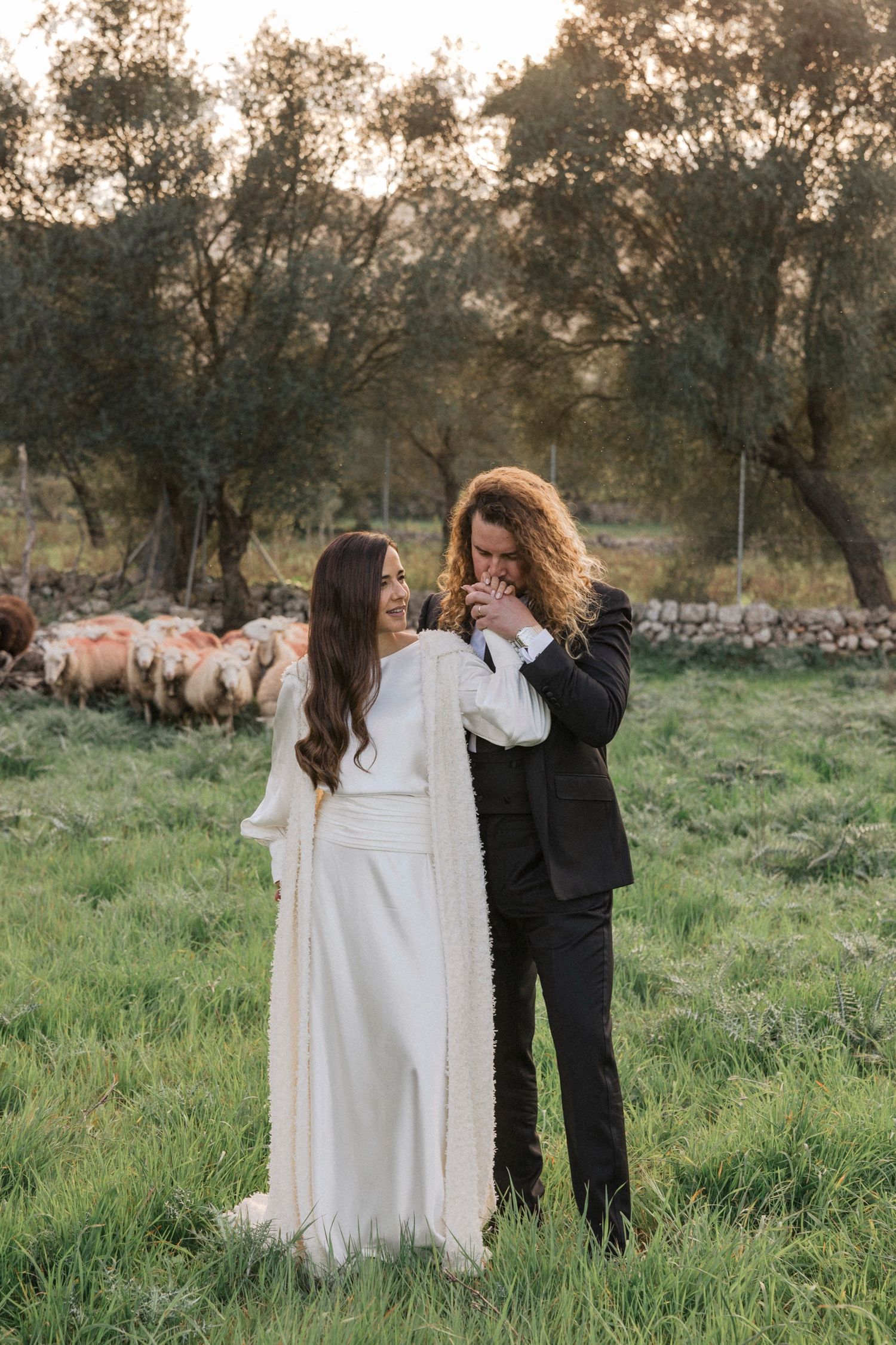 A romantic outdoor photoshoot in a grassy field with sheep grazing in the background.