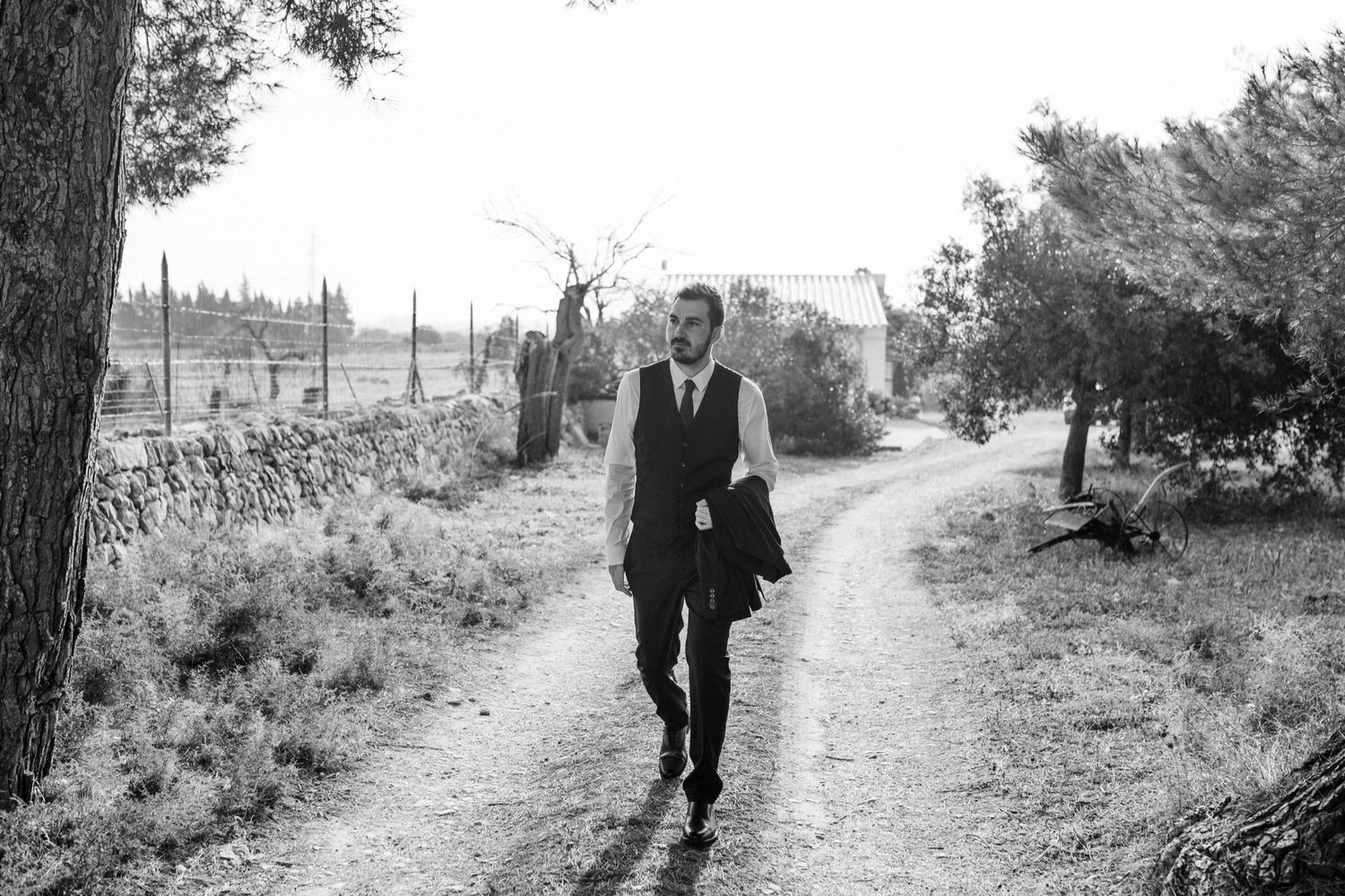 A person in formal attire walks along a rural dirt path in a black and white photograph.