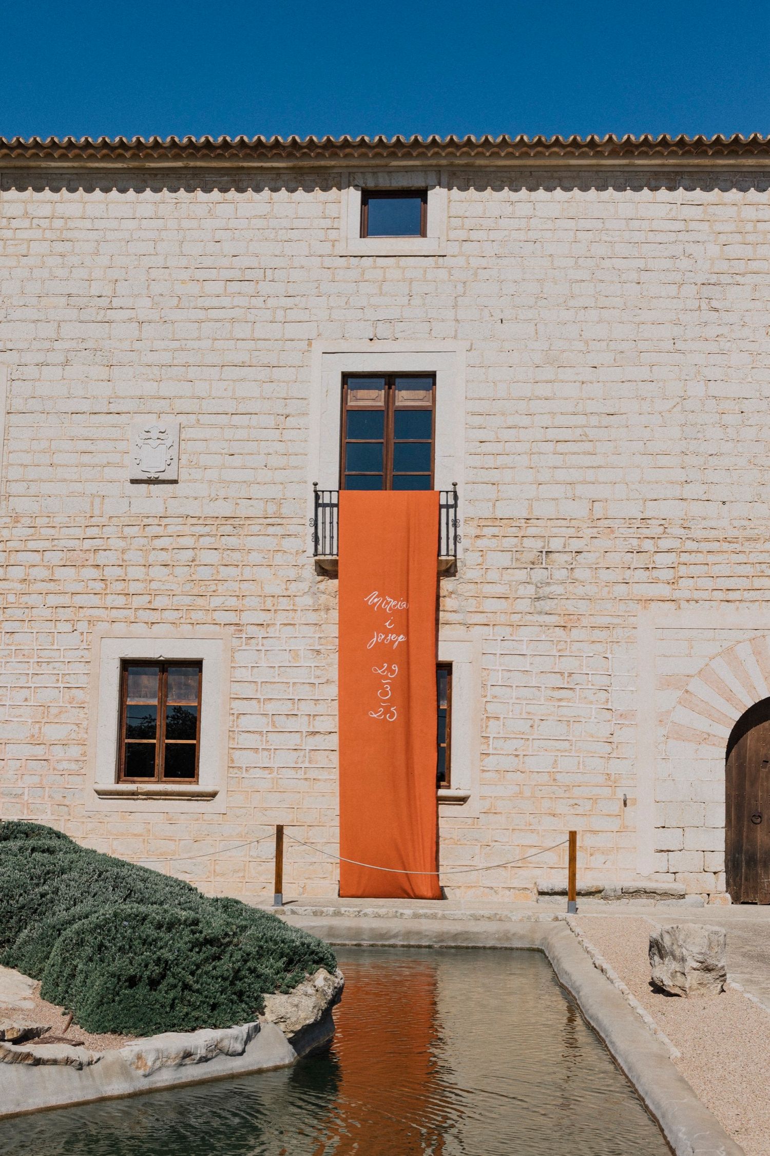 Minimalist architectural detail of white stone building with bright orange doors against blue sky.