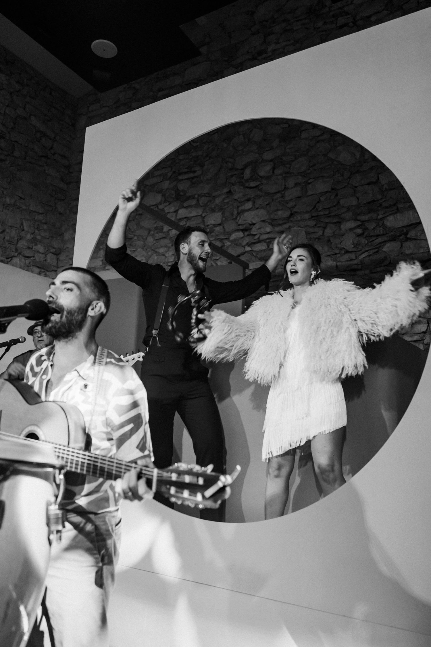 A series of black and white dance party photos showing people celebrating with arms raised and white feather boas.