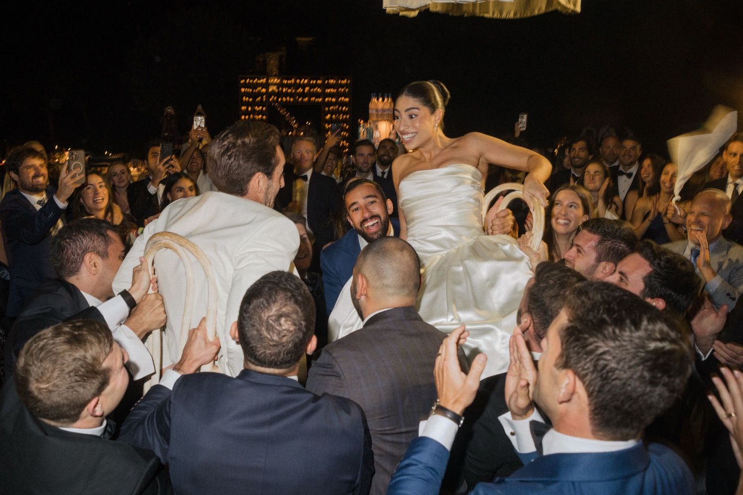Wedding guests dance and celebrate on a crowded dance floor during an evening reception.