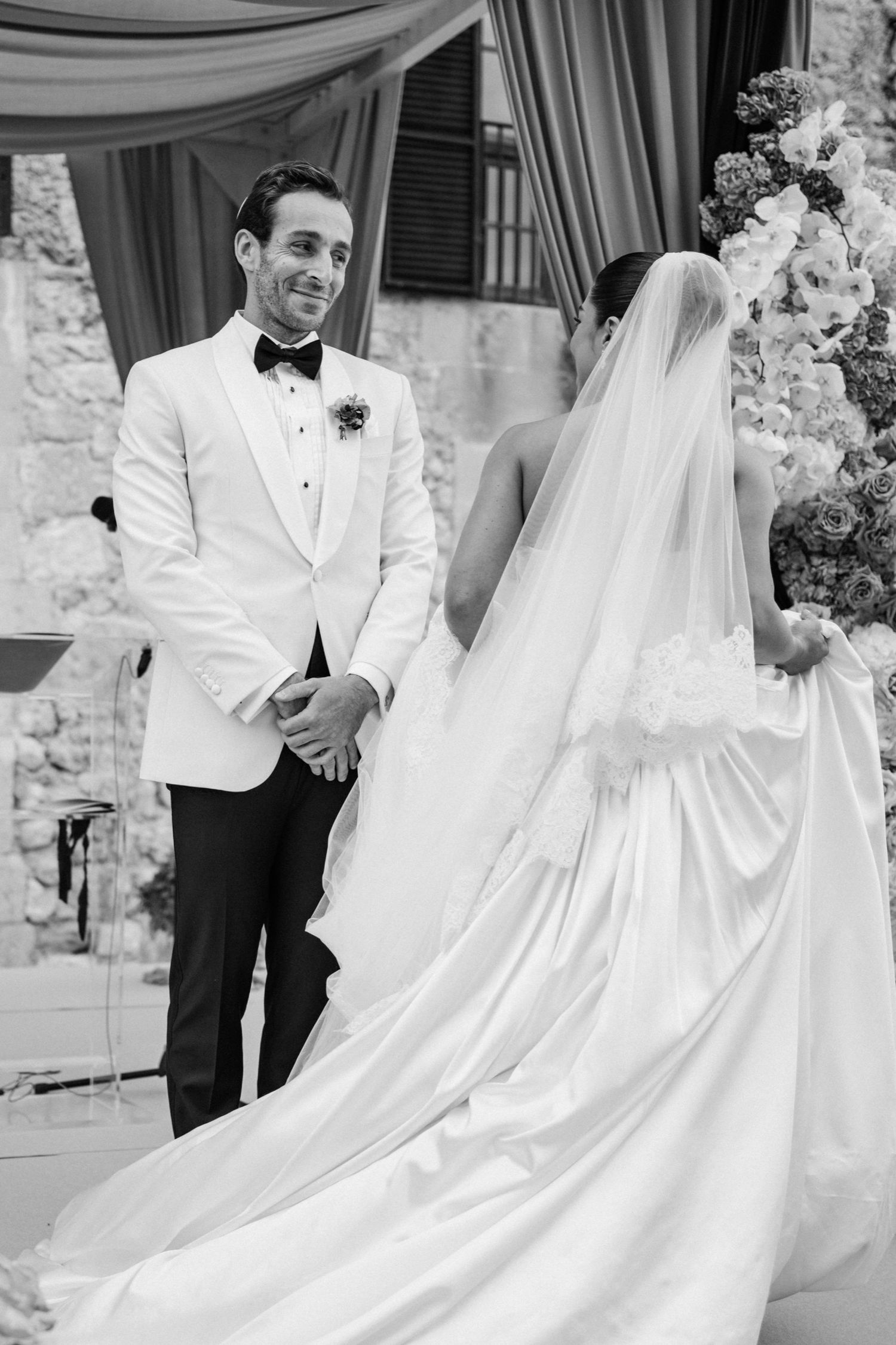 A black and white wedding photo showing a couple in formal attire with a flowing white bridal gown and veil.