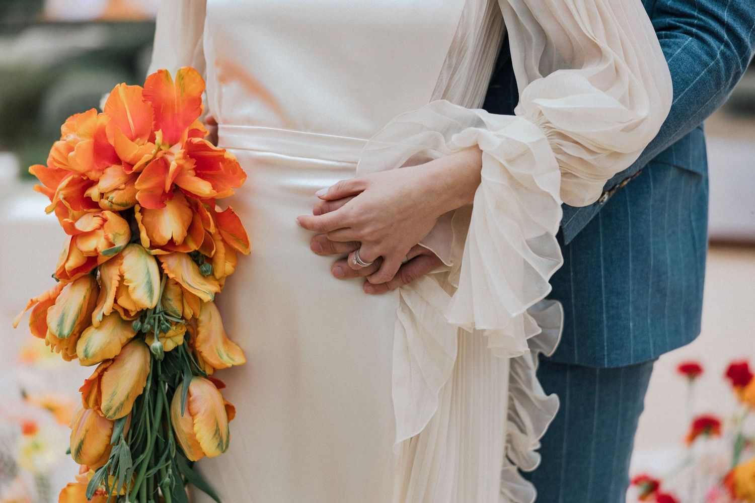 Elegant couple holding vibrant orange lily bouquets in a romantic wedding scene.