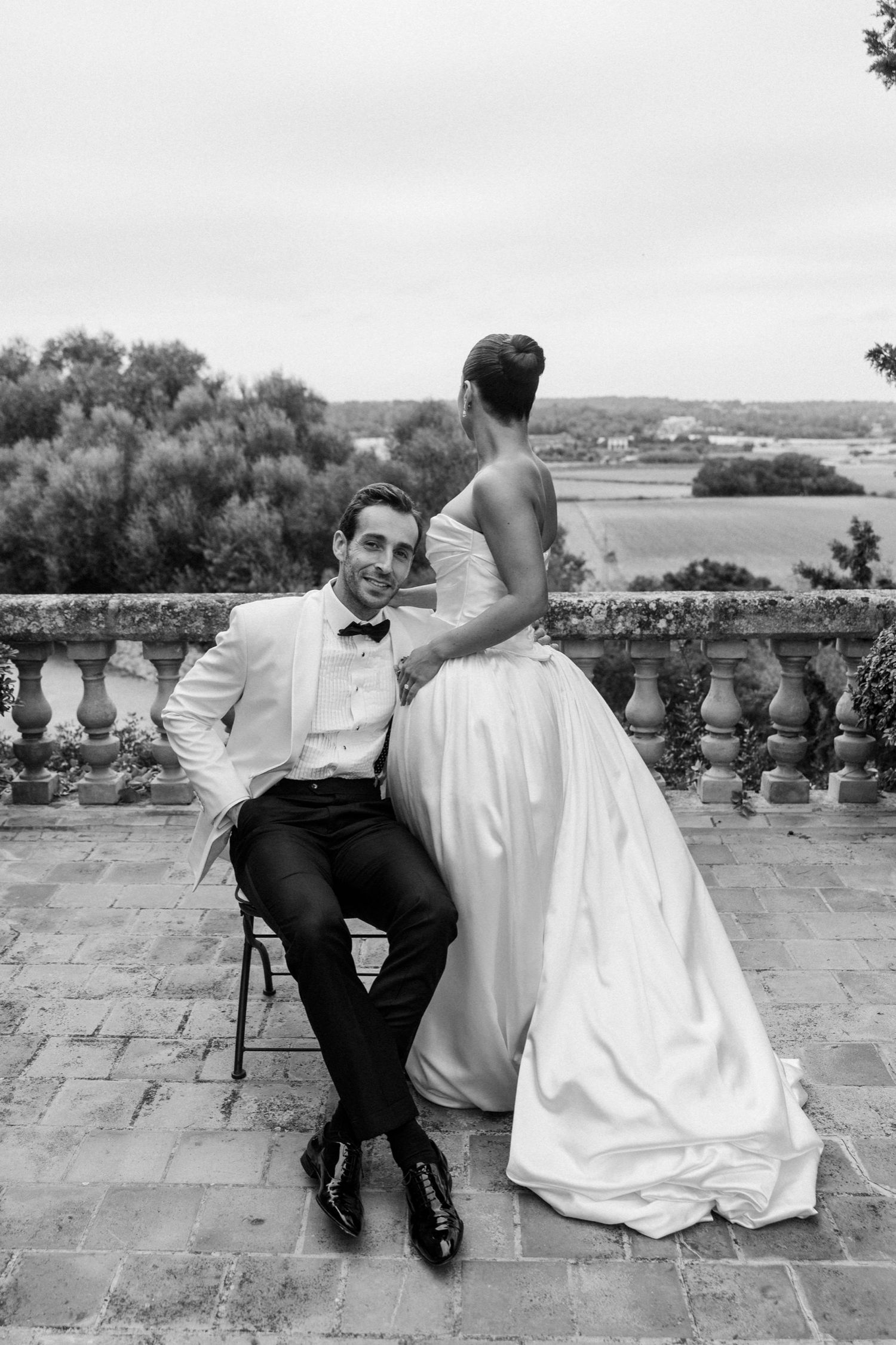 A romantic black and white portrait on a stone terrace overlooking a coastal view.