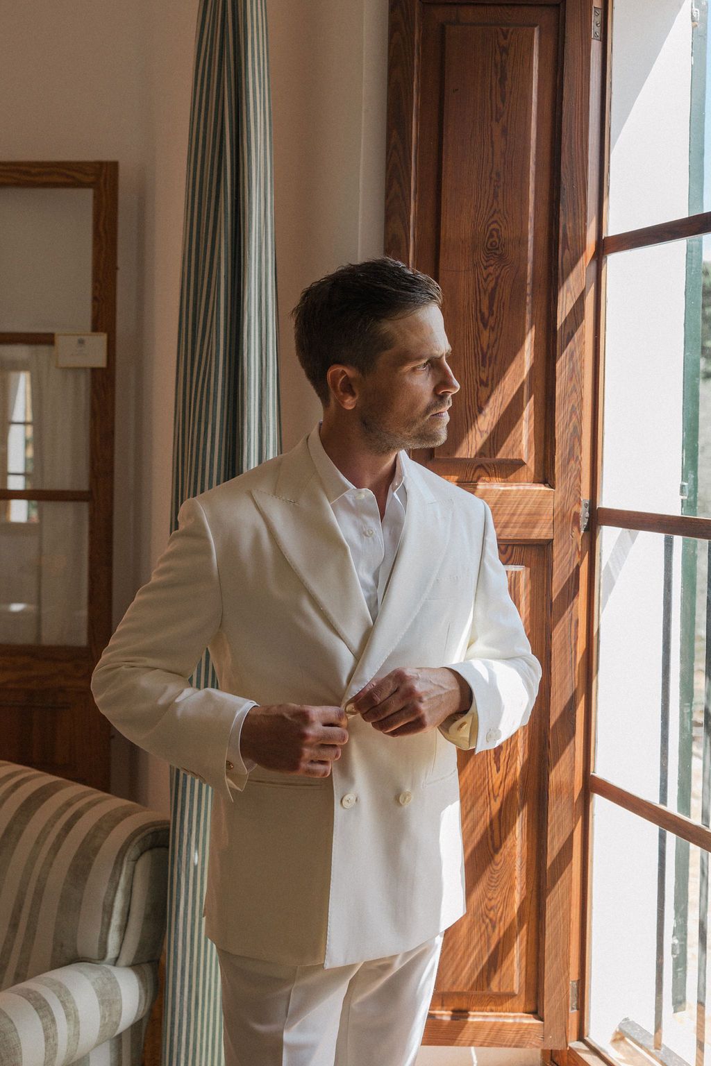 A formal white dinner jacket being worn in an elegant room with natural window lighting.