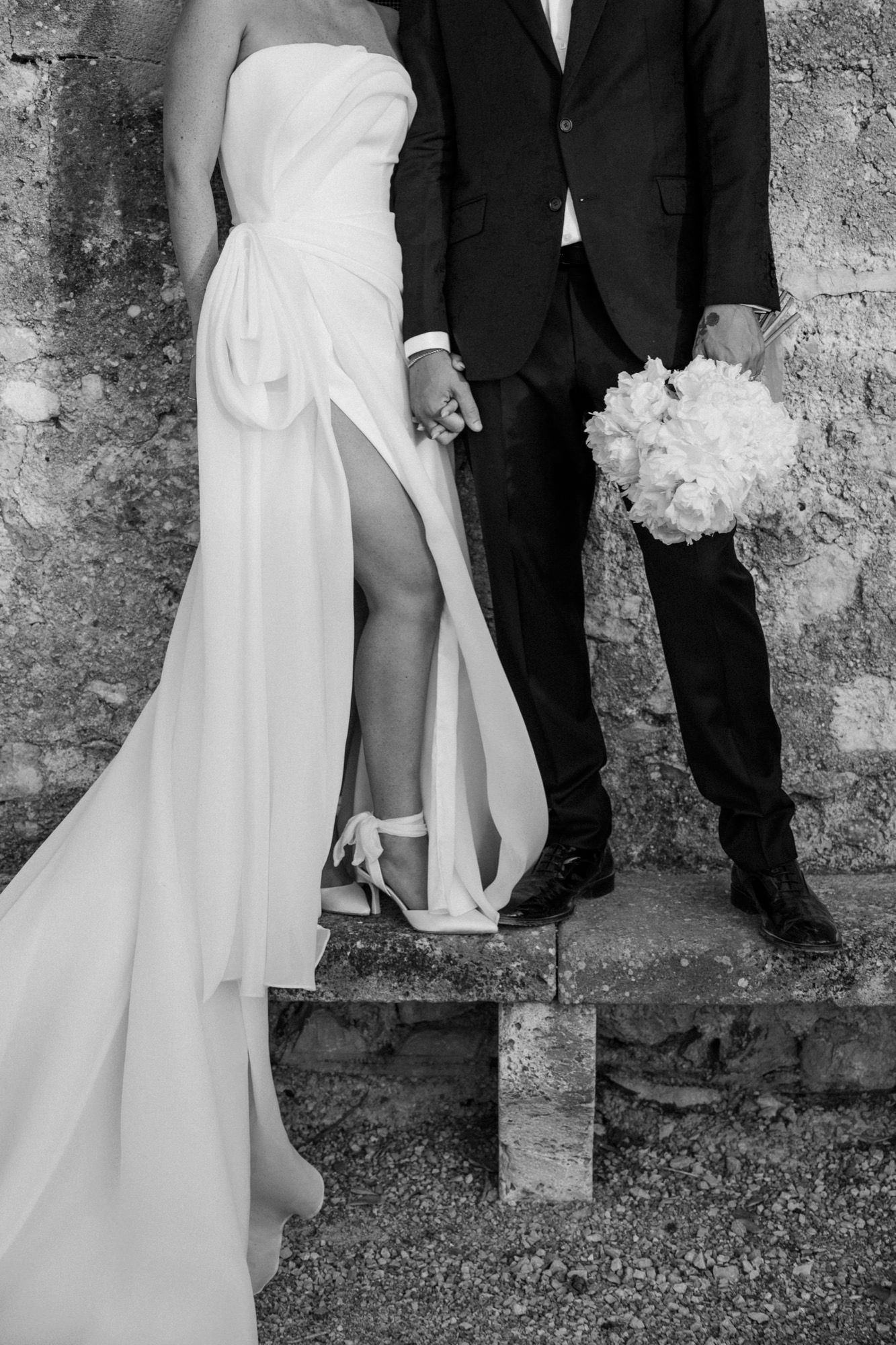 Artistic wedding photography captures bride and groom's candid moments against textured stone background.