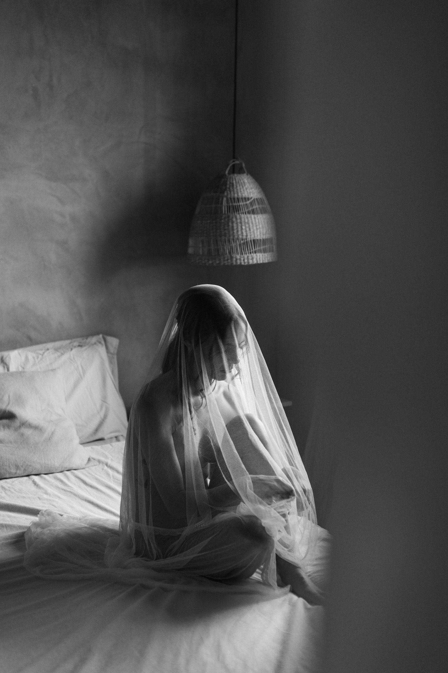 A haunting black and white series of a ghostly figure draped in fabric sitting against a wall in dim lighting.