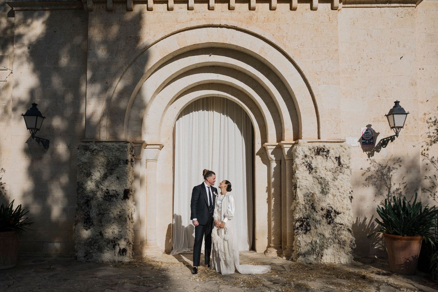 Wedding couple photographed in distance through series of stone archways with dramatic lighting.
