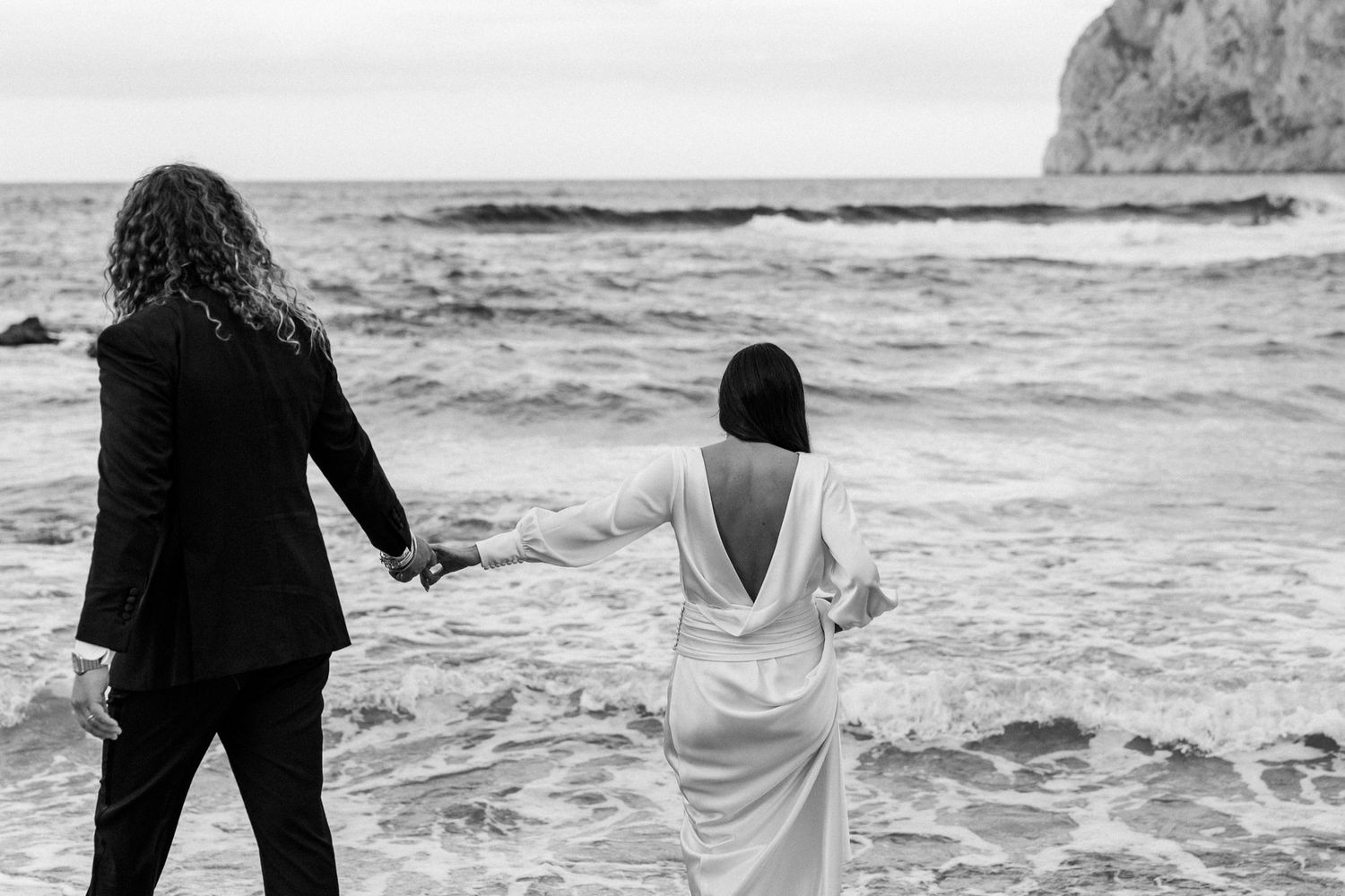 Silhouettes of people walking on a beach with dramatic coastal cliffs and waves.