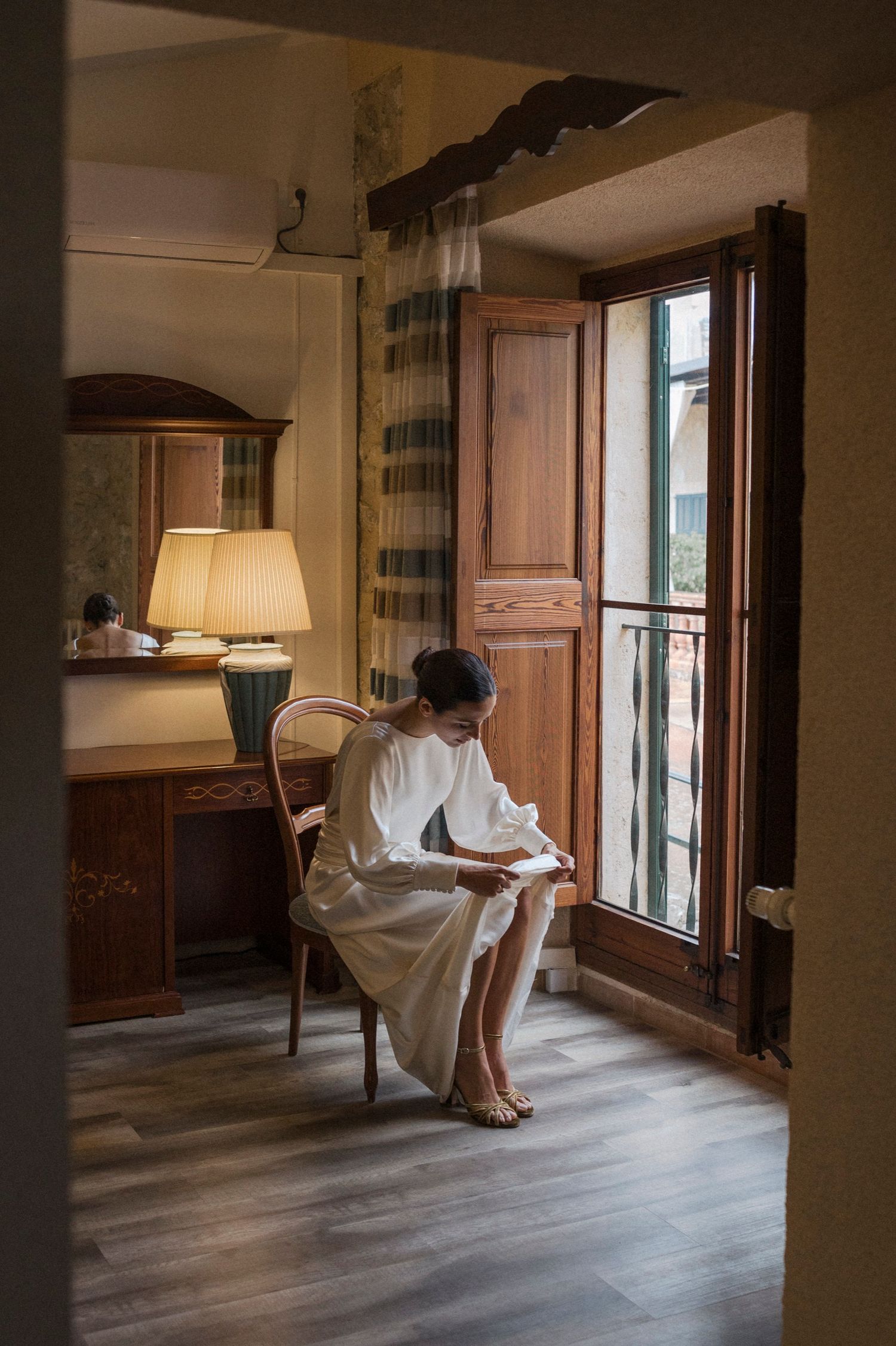 Sunlight streams through windows as someone in a white dress poses in a rustic interior space.