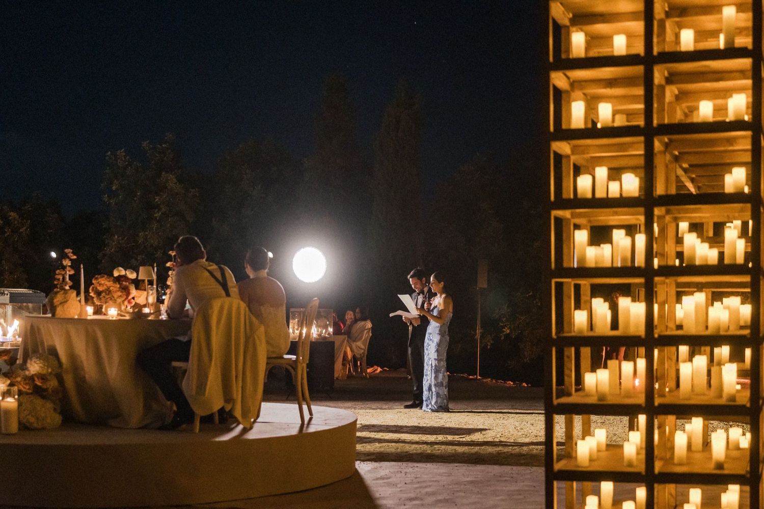 A romantic outdoor wedding setup at night with glowing candles and string lights creating a magical ambiance.