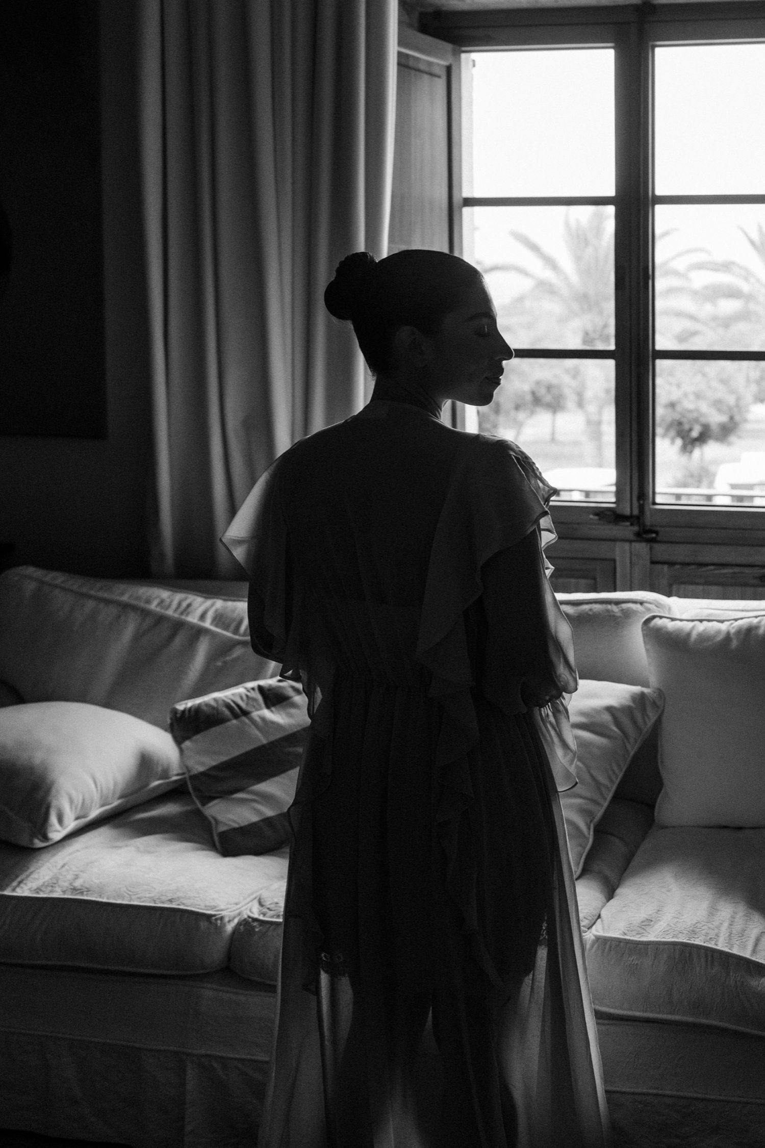 A silhouetted figure stands by a window in a moody black and white photo series showing different contemplative poses.