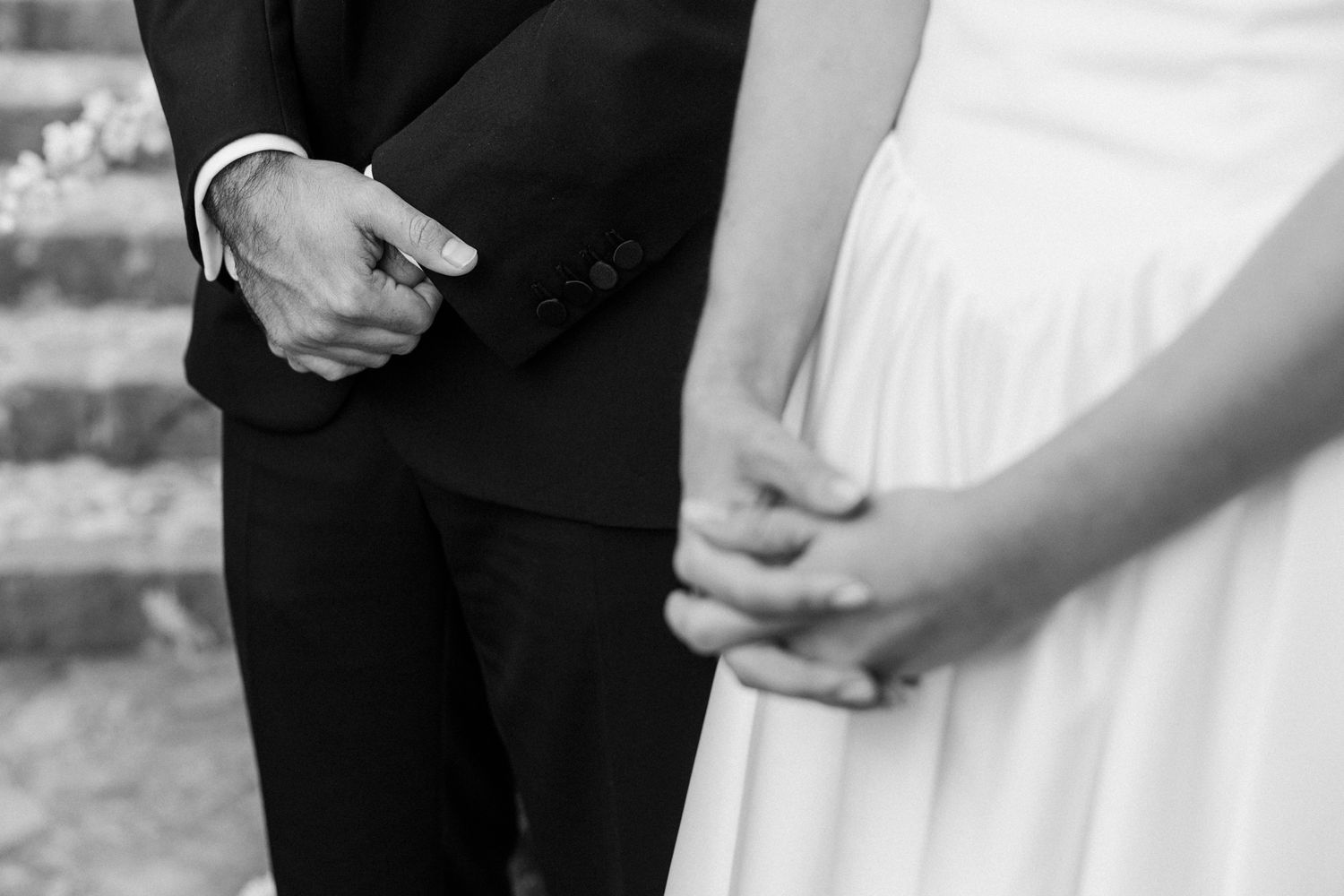 Black and white close-up of a bride and groom's hands clasped together during a wedding ceremony.