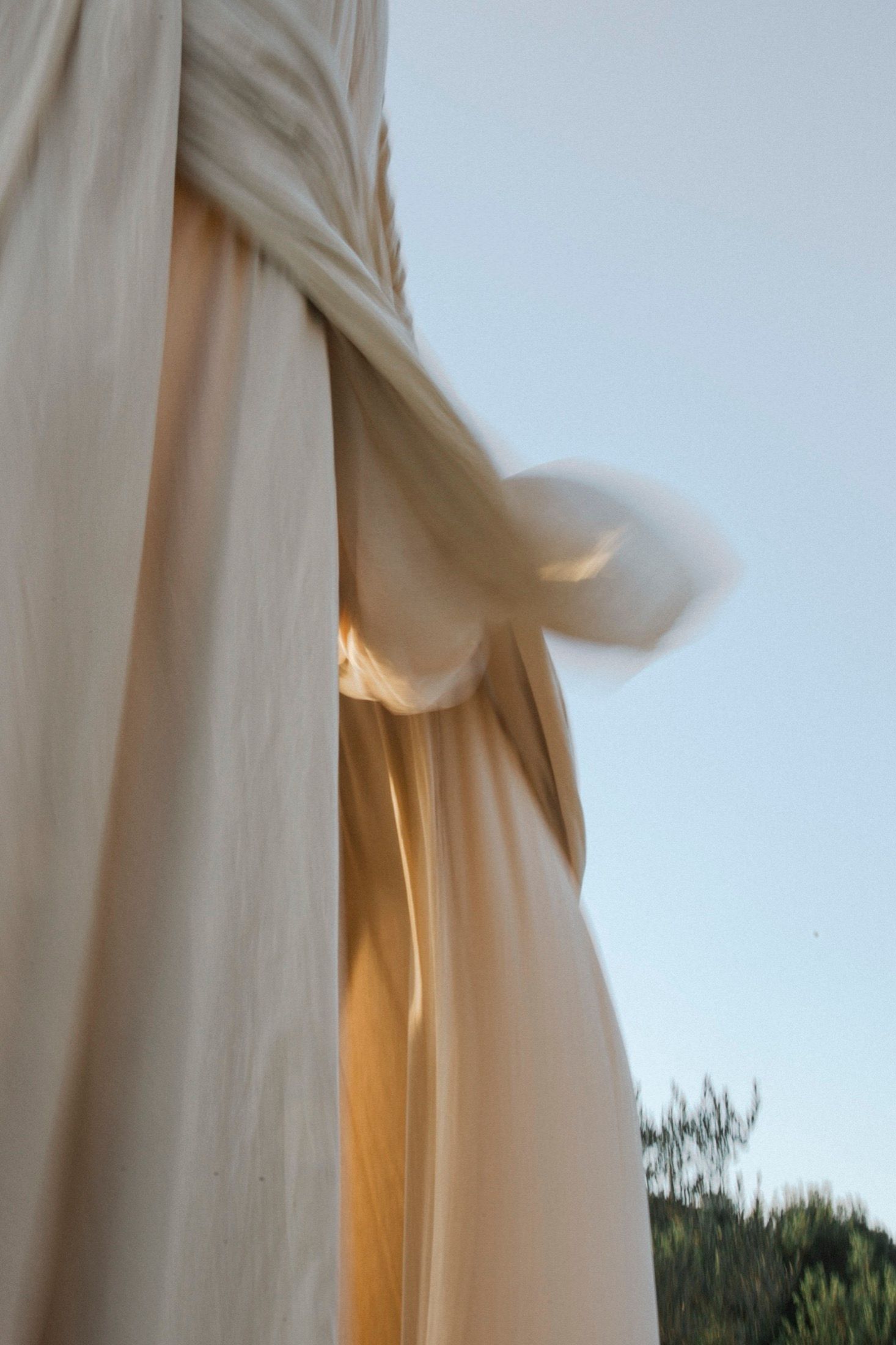 White curtains gently blowing in the breeze against a window with trees visible outside at dusk.