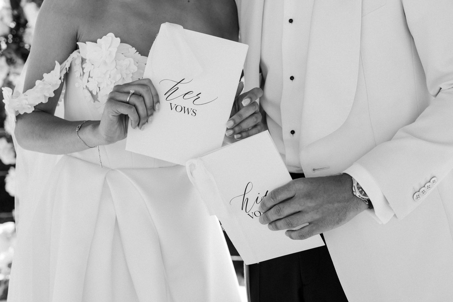 Black and white photo of bride and groom holding wedding vow booklets during outdoor ceremony.