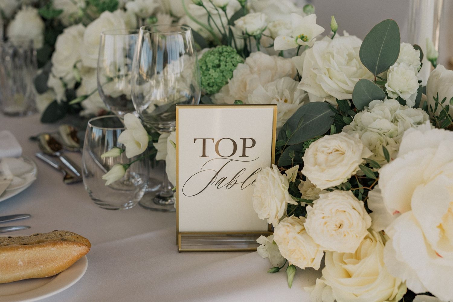 Elegant wedding top table with white roses, eucalyptus, and a gold-framed sign reading Top Table.