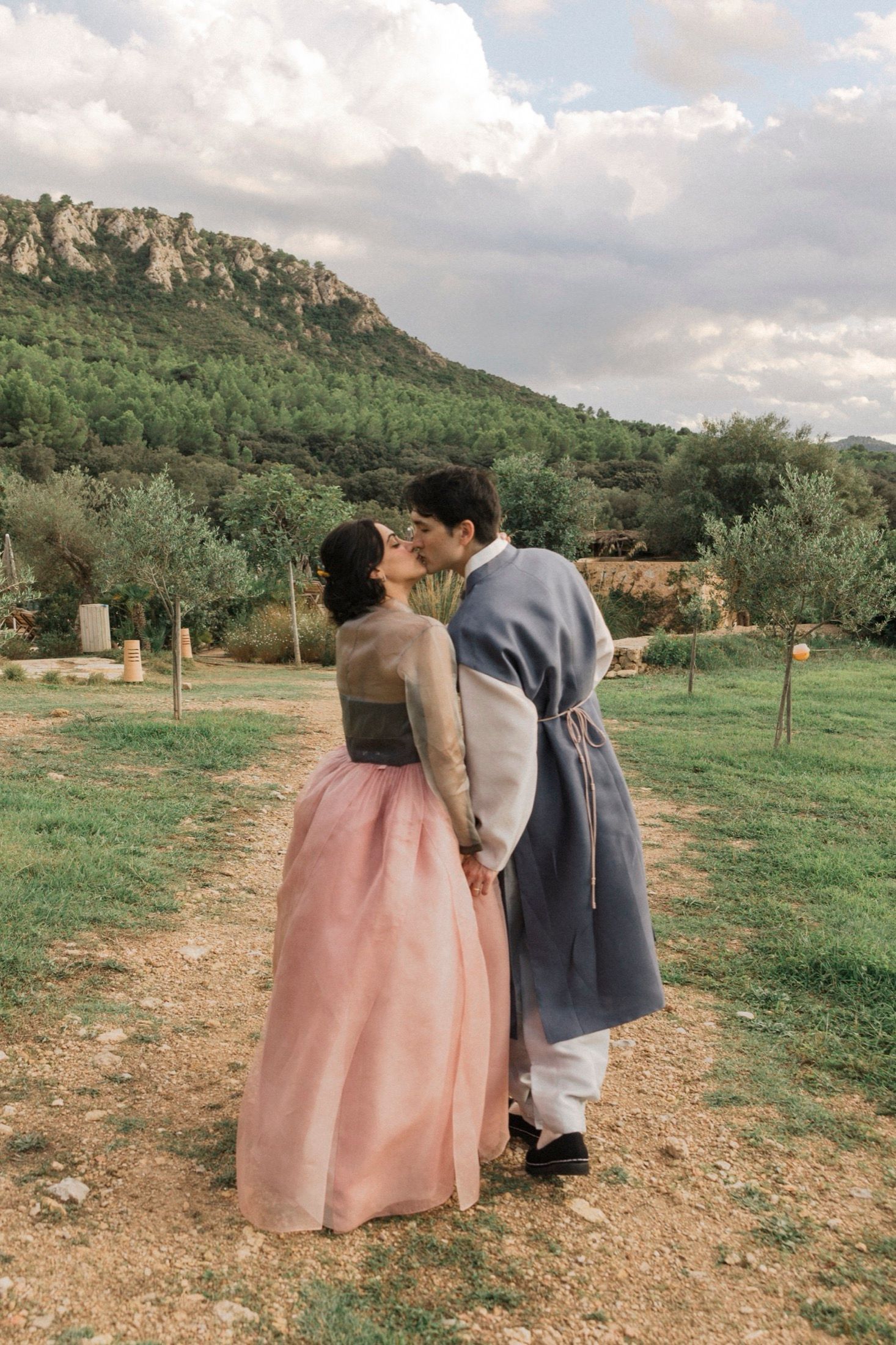 A romantic couple in formal attire shares tender moments in a scenic mountain field during a photo session.