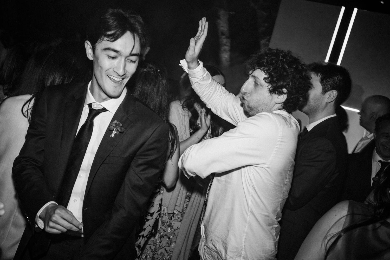 Black and white photo of people at a party with one person smiling and another raising their hand in celebration.