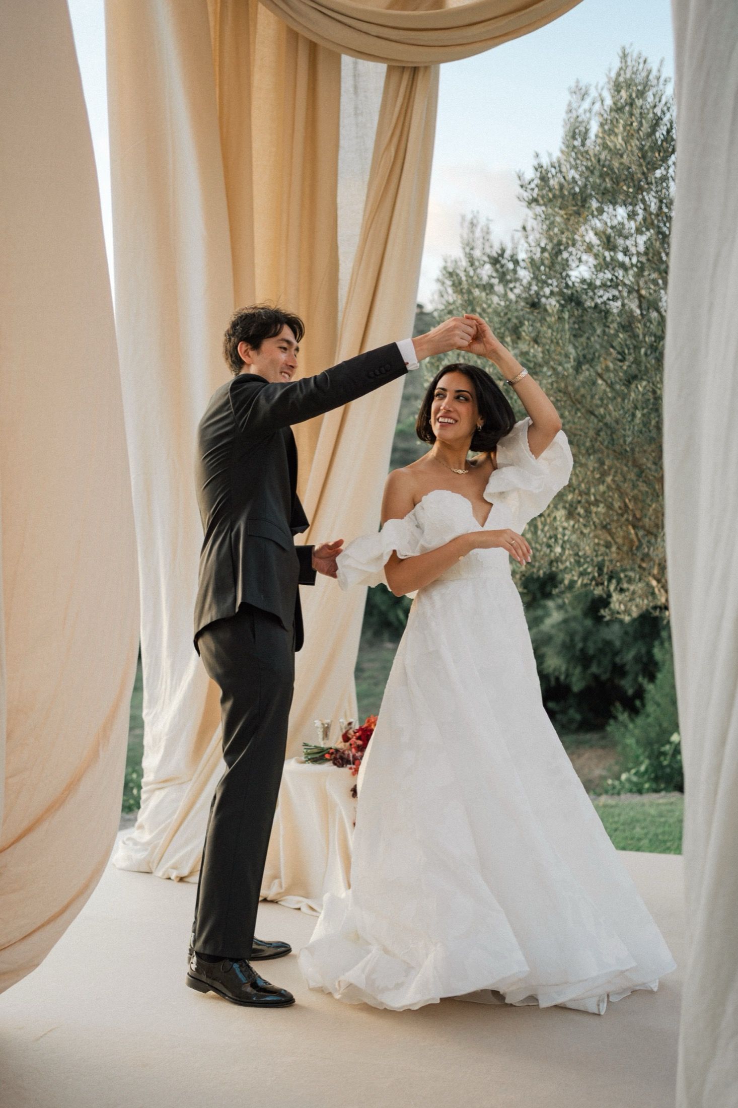Bride and groom share a romantic dance together under flowing white curtains at an outdoor wedding venue.