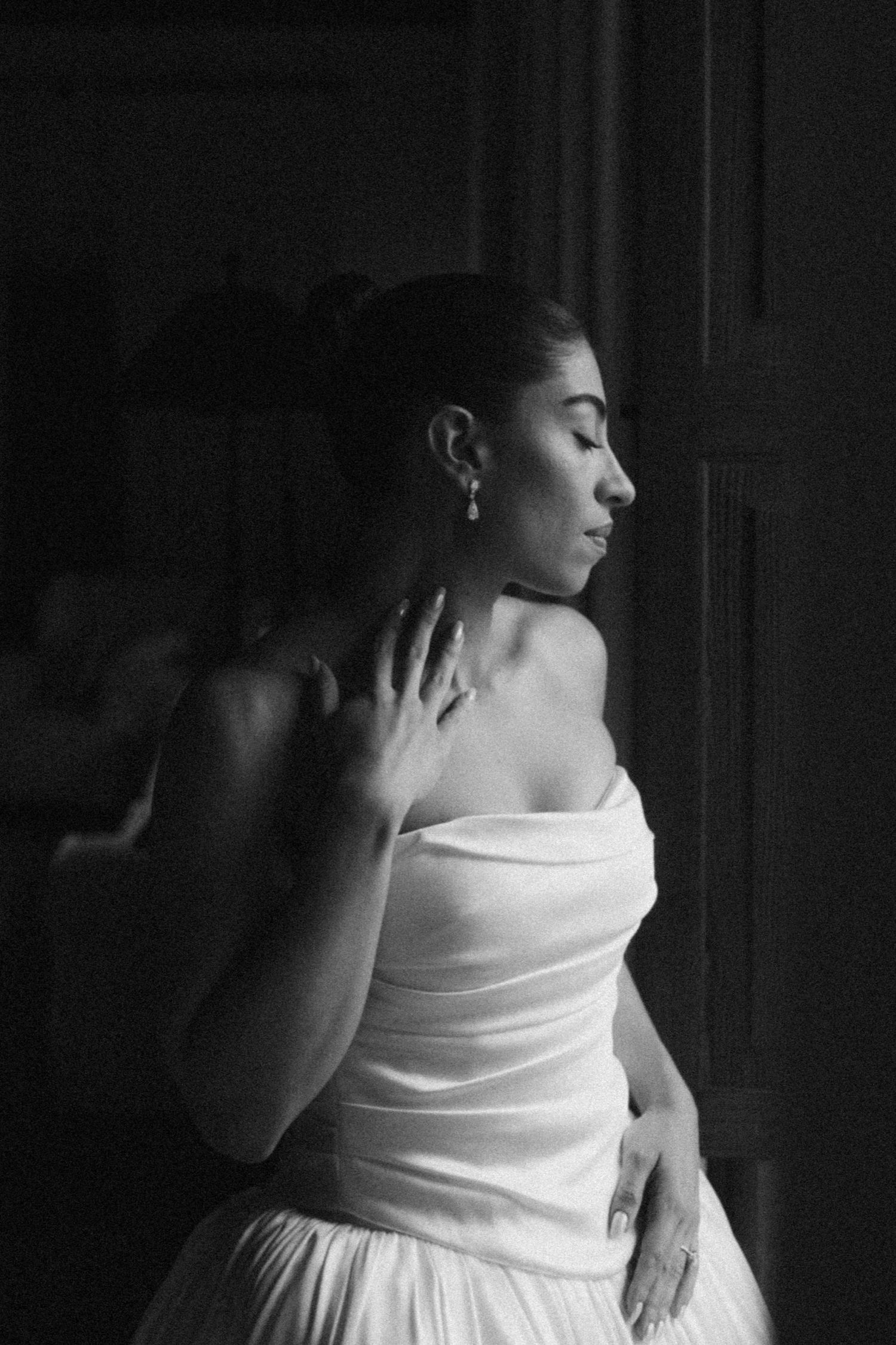 A person in a white strapless dress poses gracefully in dramatic black and white lighting.