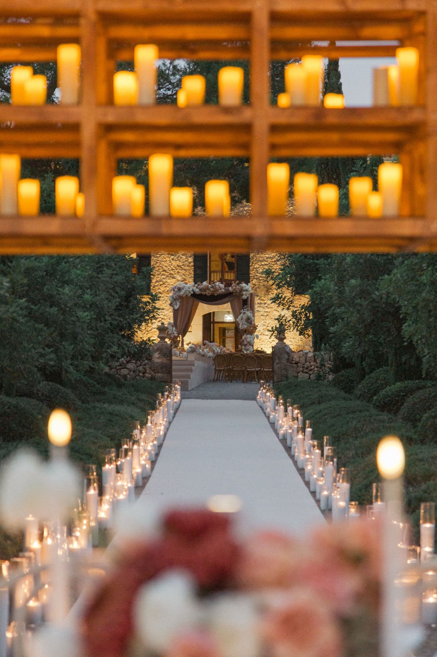 Outdoor wedding aisle lined with glowing candles and lanterns creating a romantic illuminated pathway at dusk.
