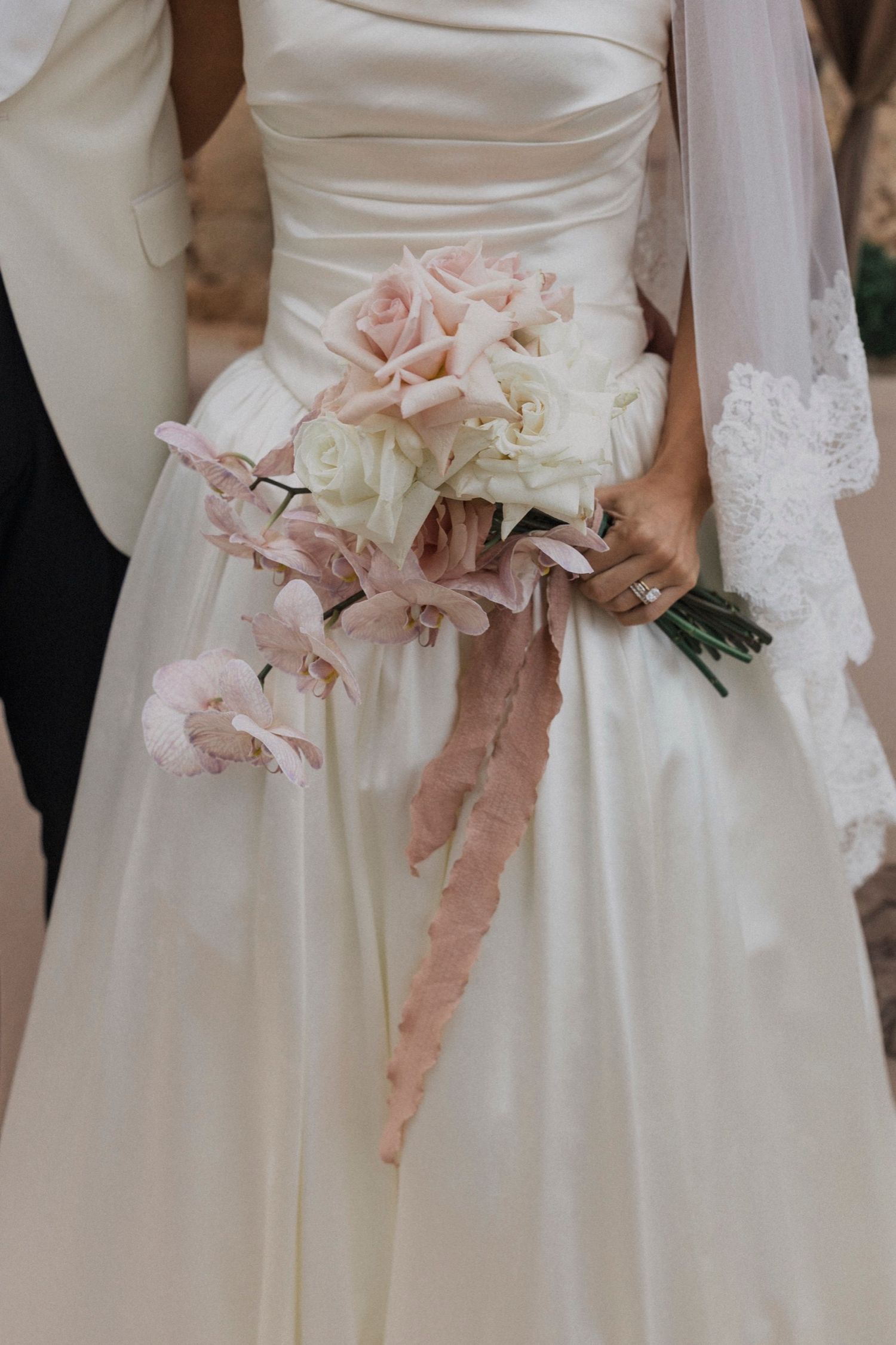 A bride in a white wedding gown holds a delicate bouquet of blush pink flowers with trailing ribbons.
